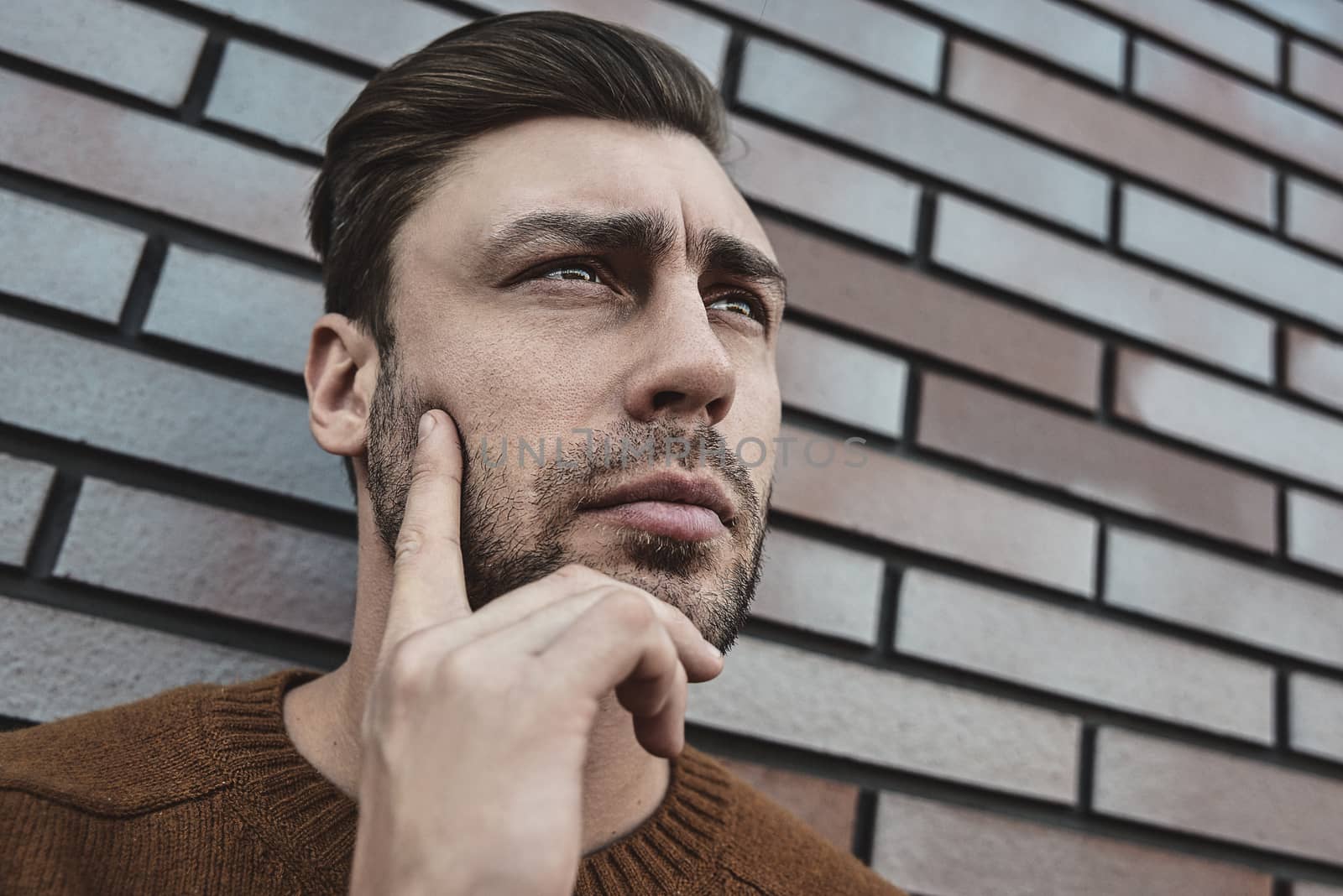 Portrait of handsome serious man thinking about something isolated on brown brick wall.