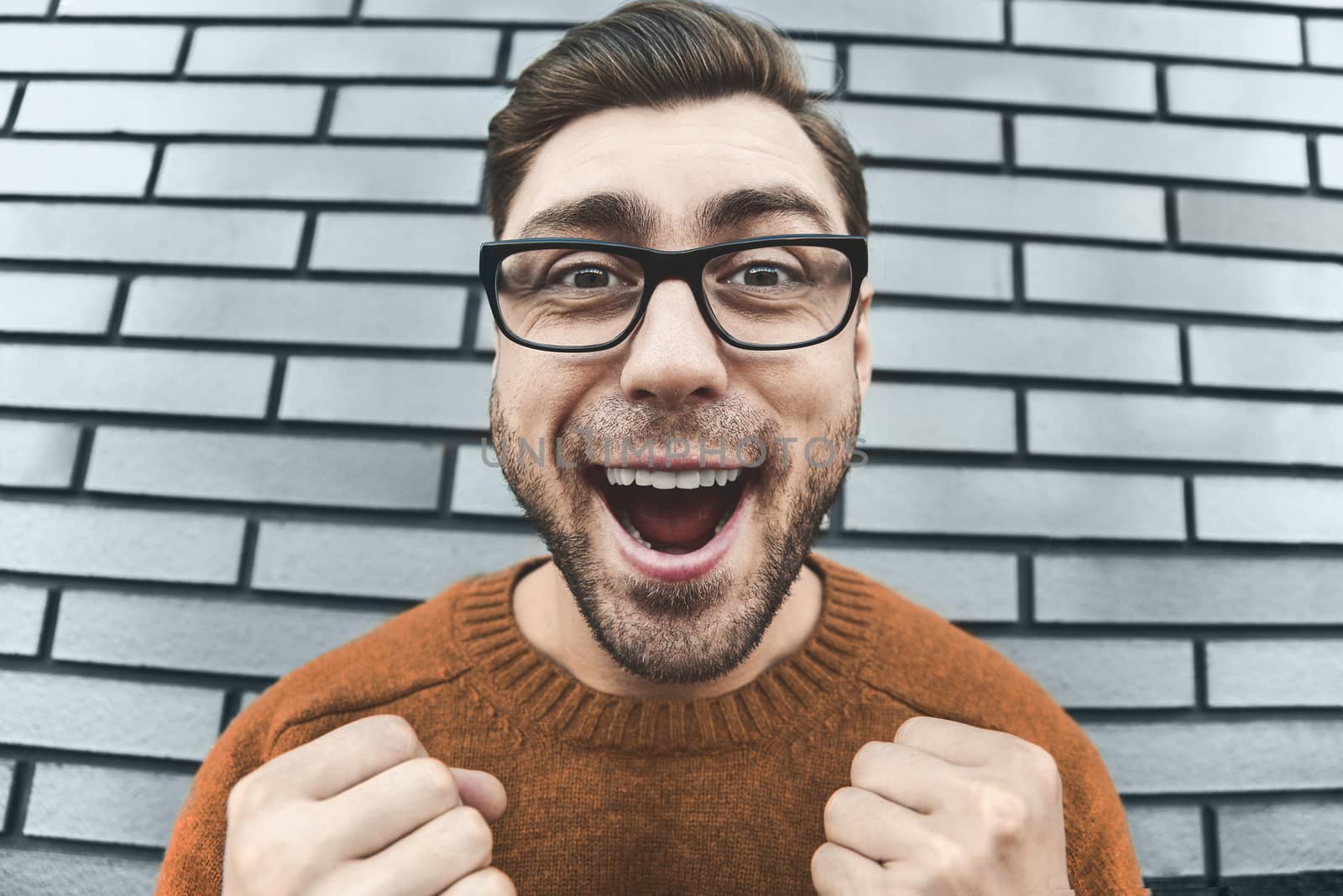 Young adult man over brown brick wall screaming proud and celebrating victory and success very excited, cheering emotion. Success concept.