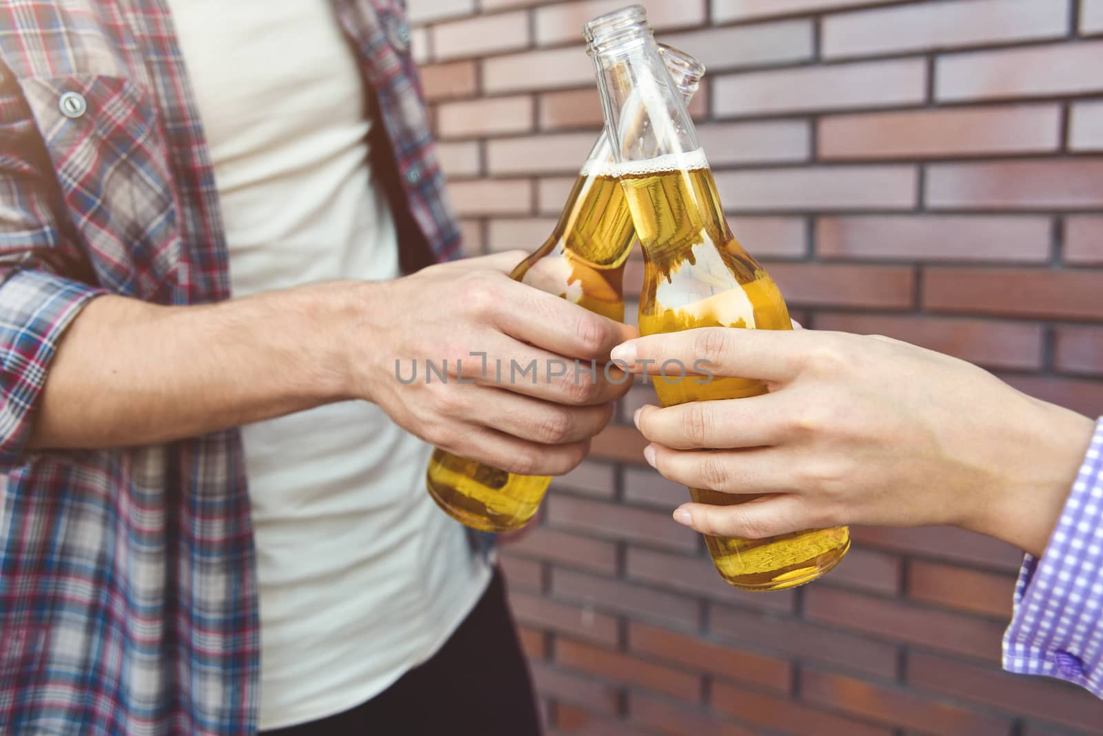 Friends enjoying with beer on a brown brick wall background.