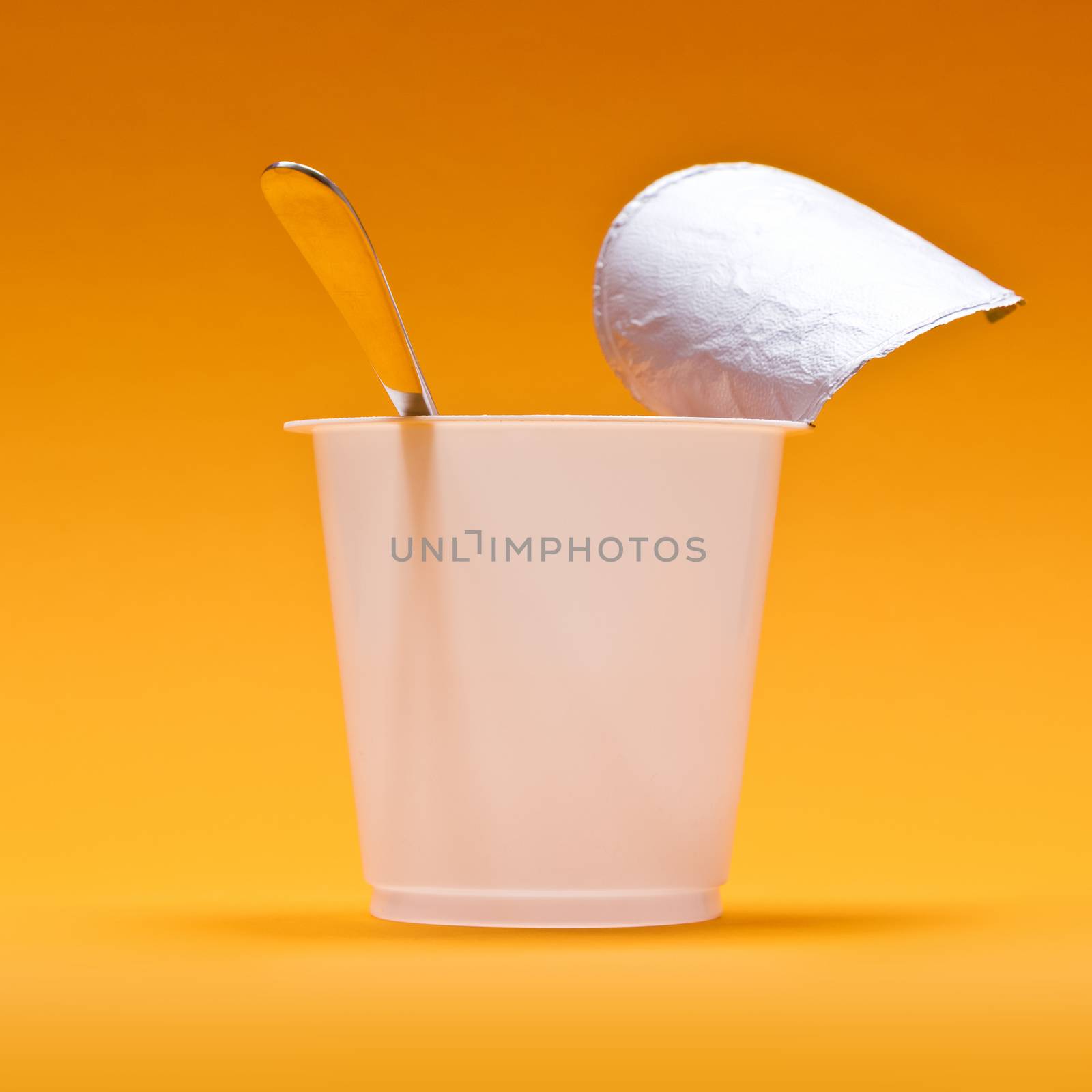 An empty clean yogurt cup with spoon on an orange background