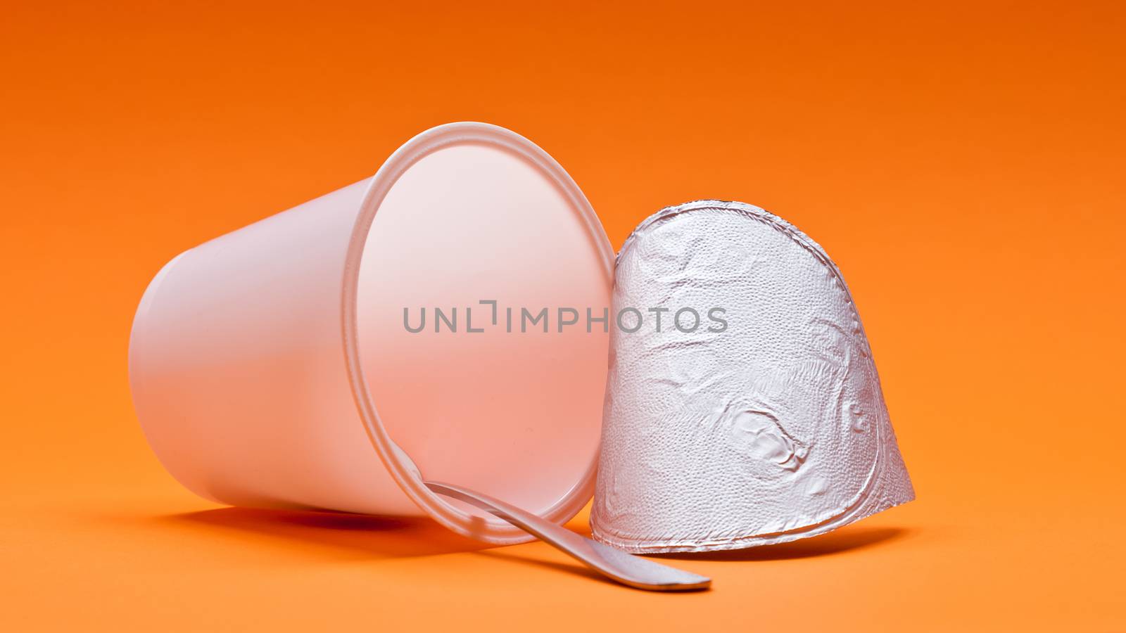 An empty clean yogurt cup with spoon on an orange background