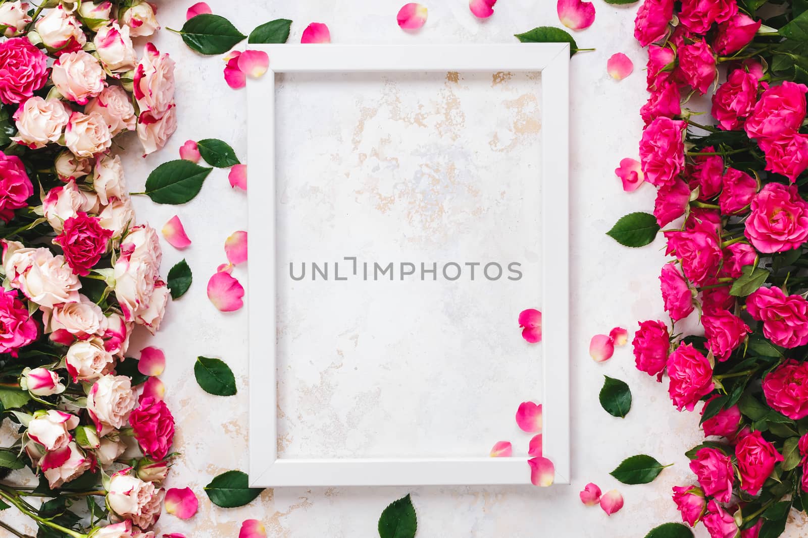Various brightly colored pink and red roses directed at each other on rustic white and gold surface and empty white wooden frame.  Top view, blank space