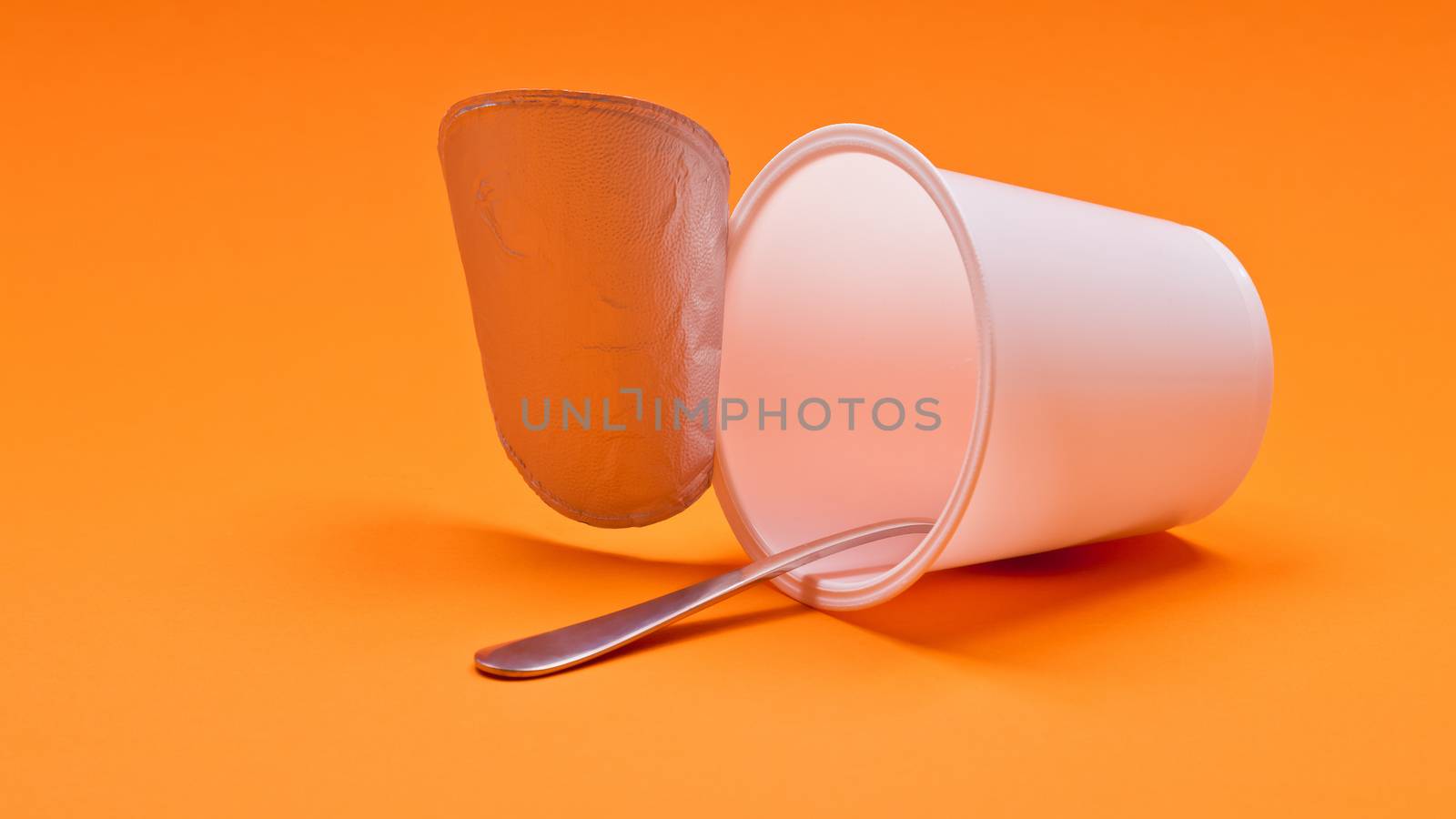 An empty clean yogurt cup with spoon on an orange background