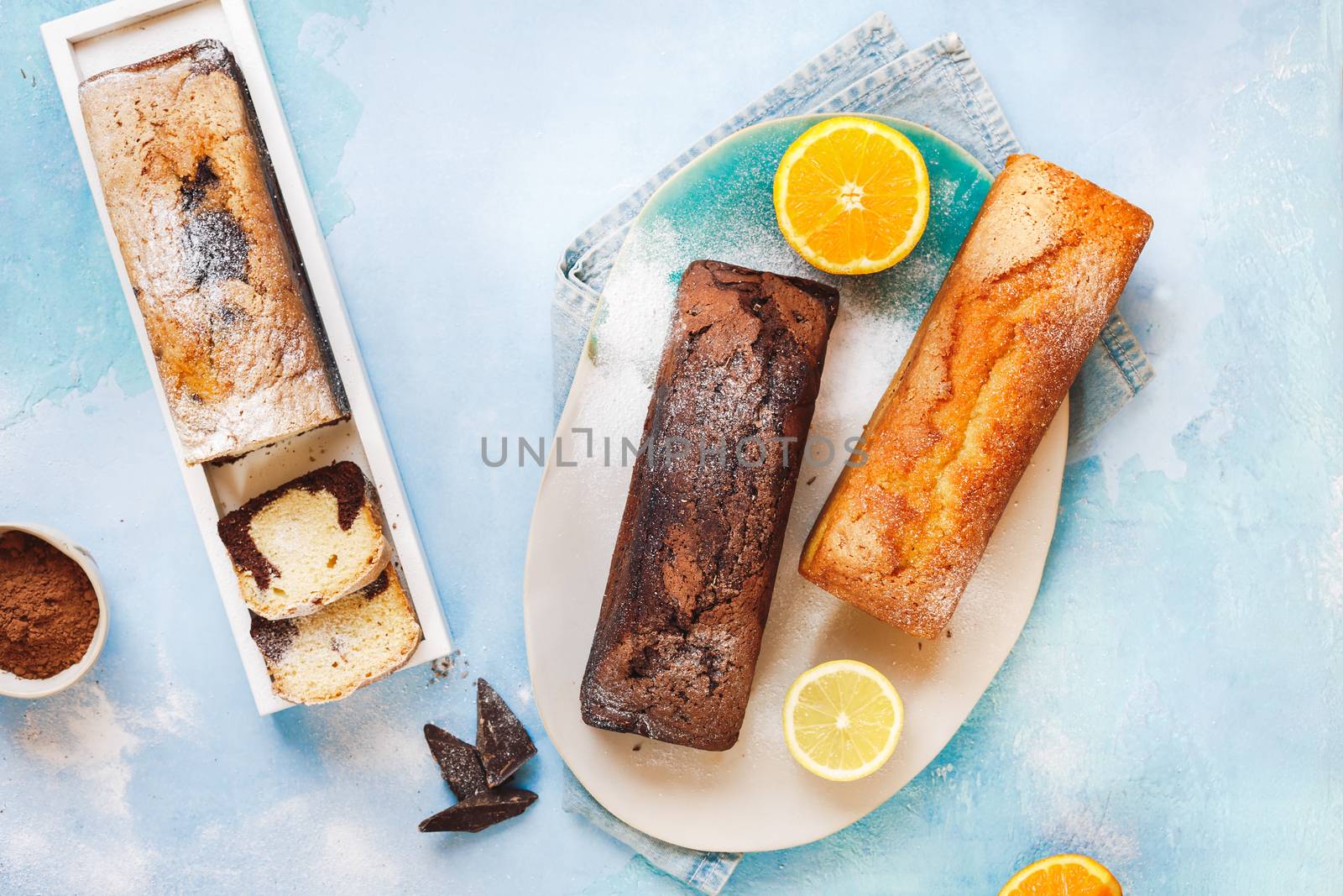 Assorted pound cakes whole and sliced into portions lying on a coloured rustic table, top view, blank space