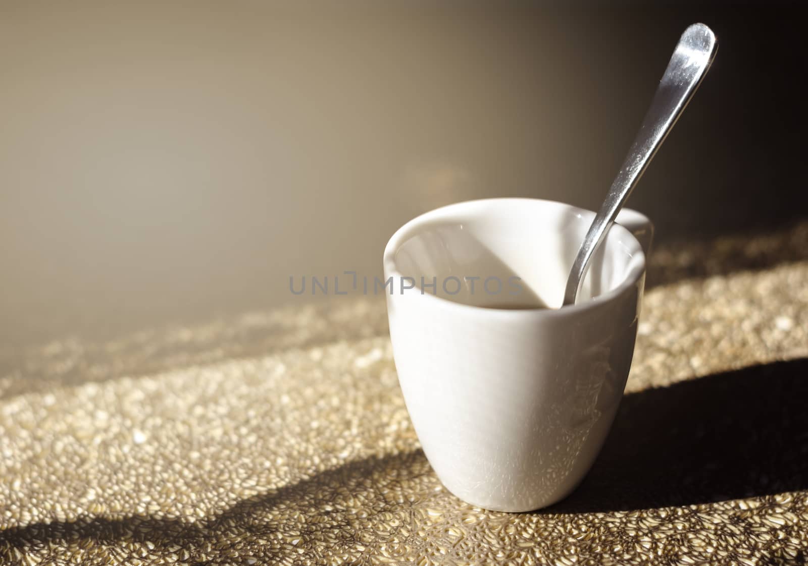 a white ceramic cup with a steel spoon filled with black coffee illuminated by natural sunlight by rarrarorro