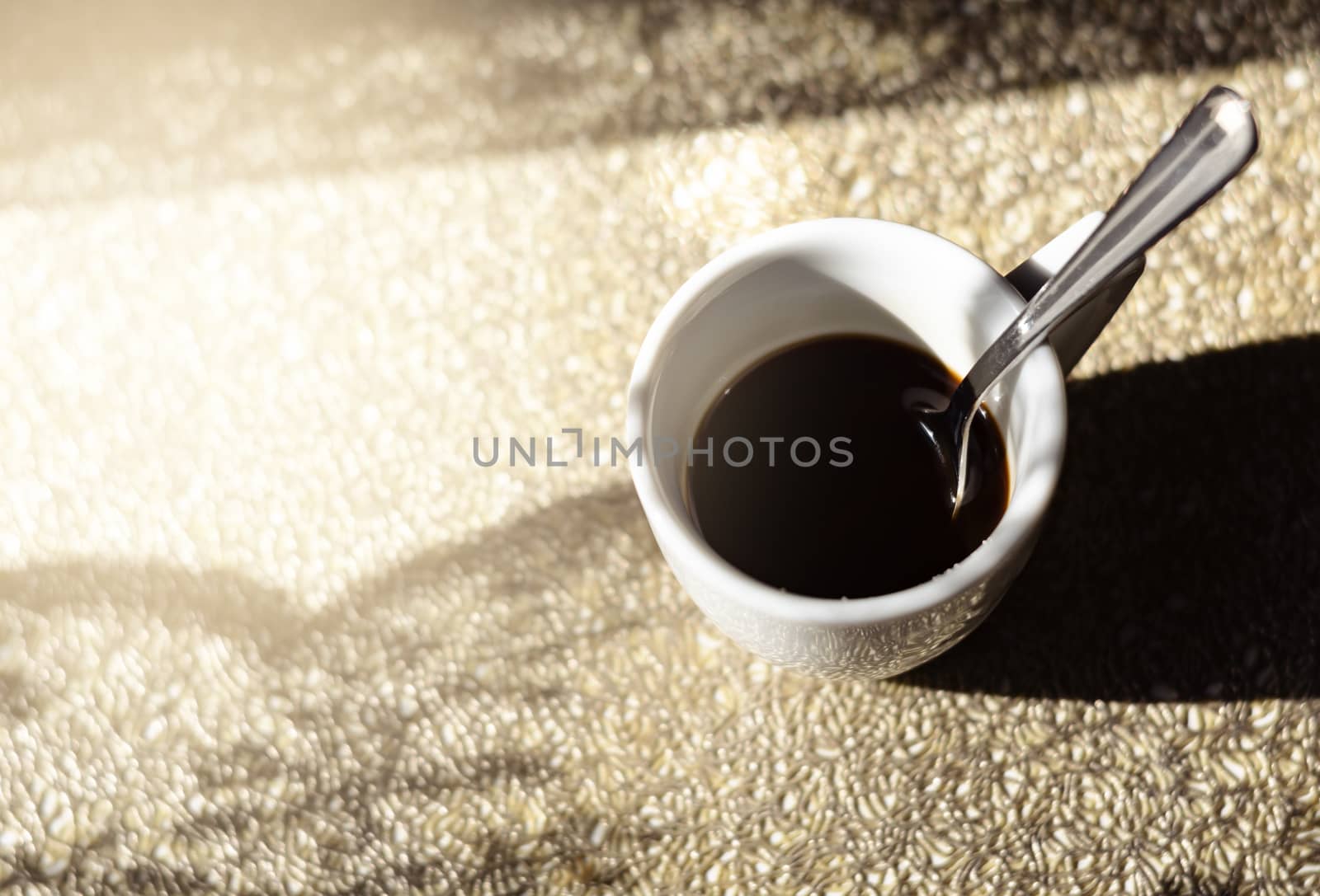 a white ceramic cup with a steel spoon filled with black coffee illuminated by natural sunlight by rarrarorro