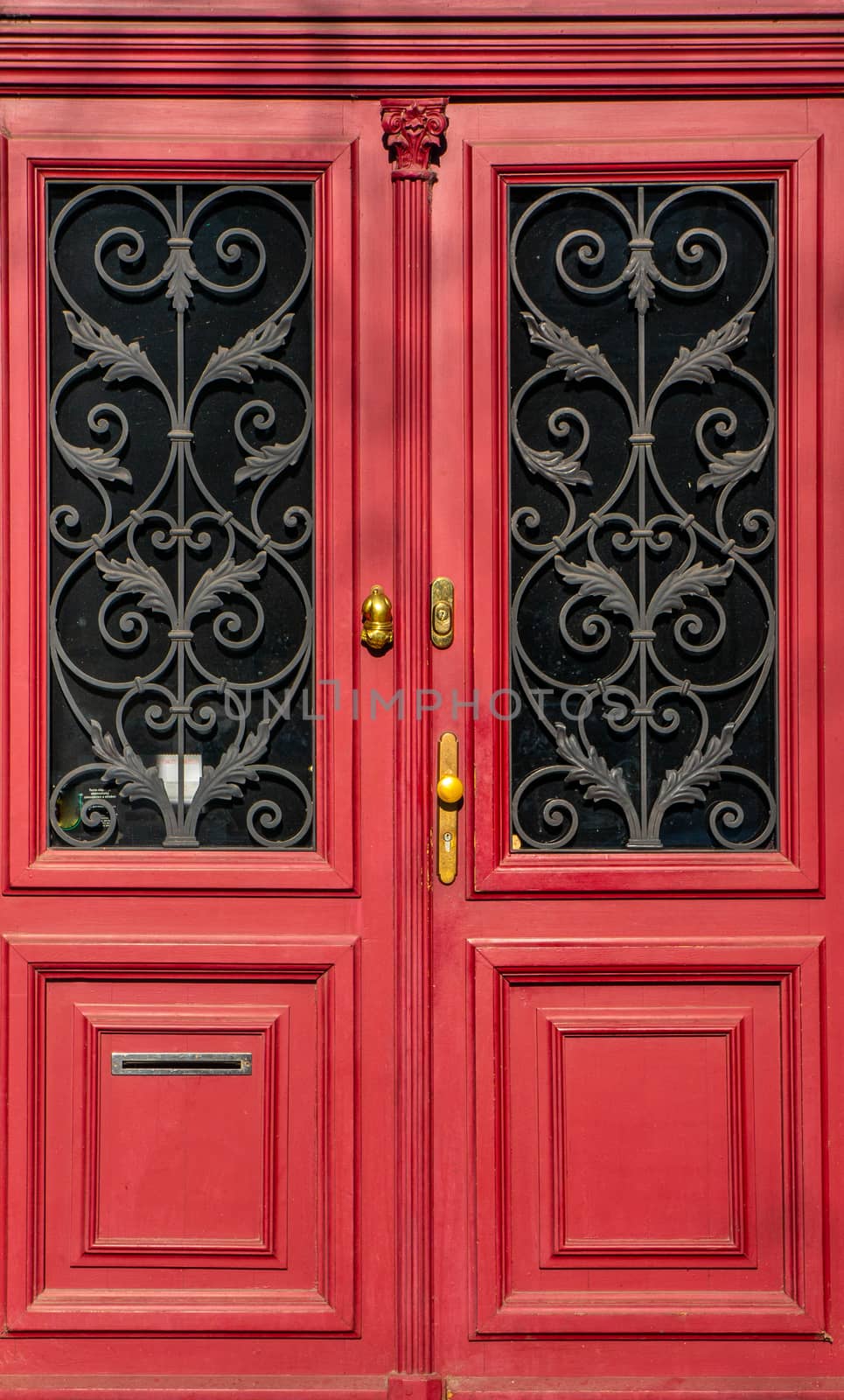 Vibrant and bold red ornate doorway. Romantically decorated brass details on dark windows and gold details. Shot in bright daylight