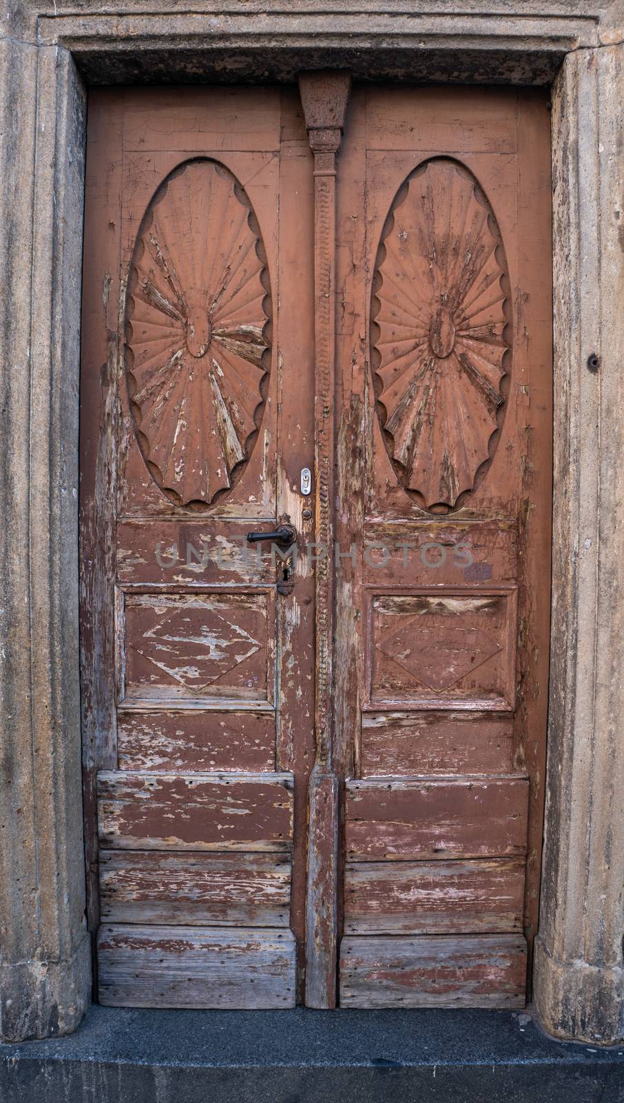 Worn out ornate brown doorway with paint chipping away in classical European architecture style, Stone steps in front and black brass details shot in natural light.