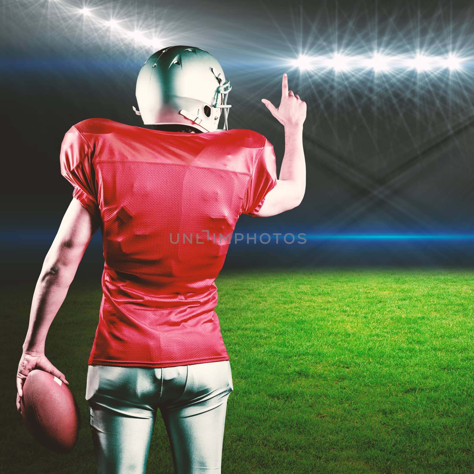 Rear view of American football player pointing while holding ball against rugby stadium