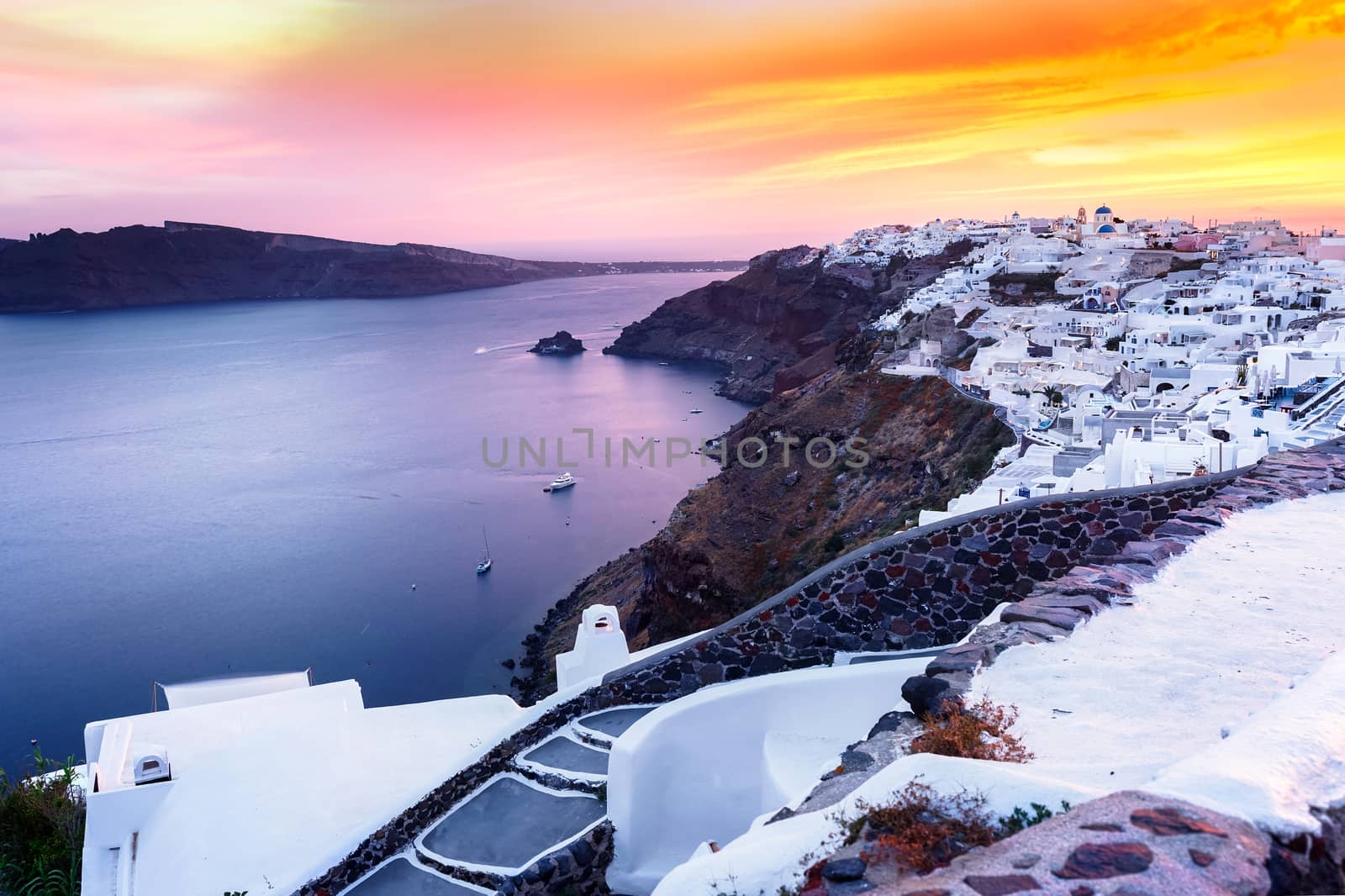 World famous Oia village at sunset, Santorini.  Caldera and traditional, famous white washed buildings and churches with blue domes over the caldera,Santorini island, Greece.