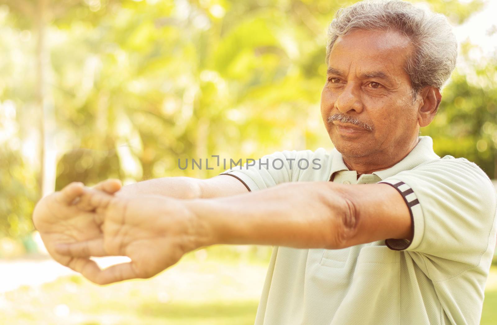 Senior man stretches hands before exercise - Concept of elderly person fitness outdoor - 60s person doing yoga asana at park