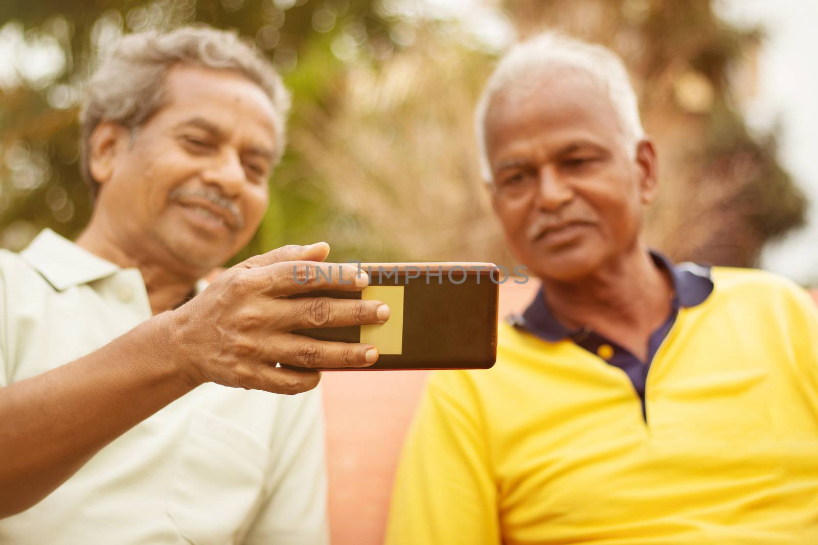 Selective focus on phone two Happy older men busy in watching mobile outdoor - concept of senior people using technology - Two mature old friends having fun at park. by lakshmiprasad.maski@gmai.com