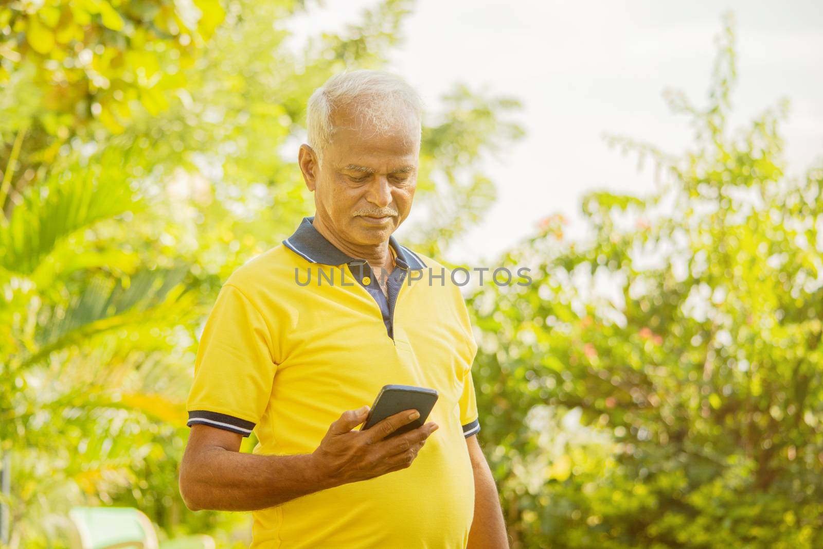 senior man looking the phone - old male person using mobile at park - elderly citizen on smartphone outdoor