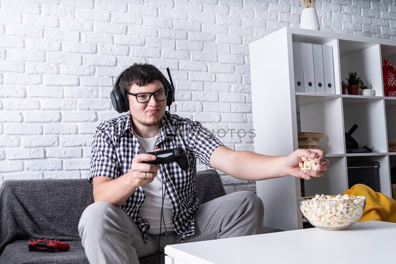 young man playing video games at home eating popcorn by Desperada