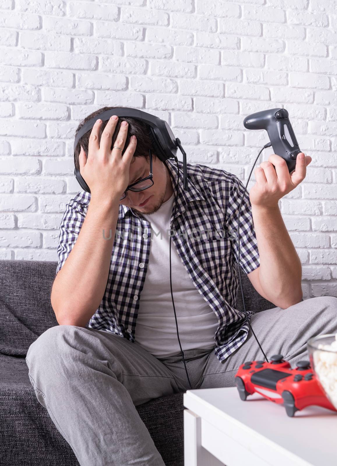 Disappointed young man playing video games at home by Desperada