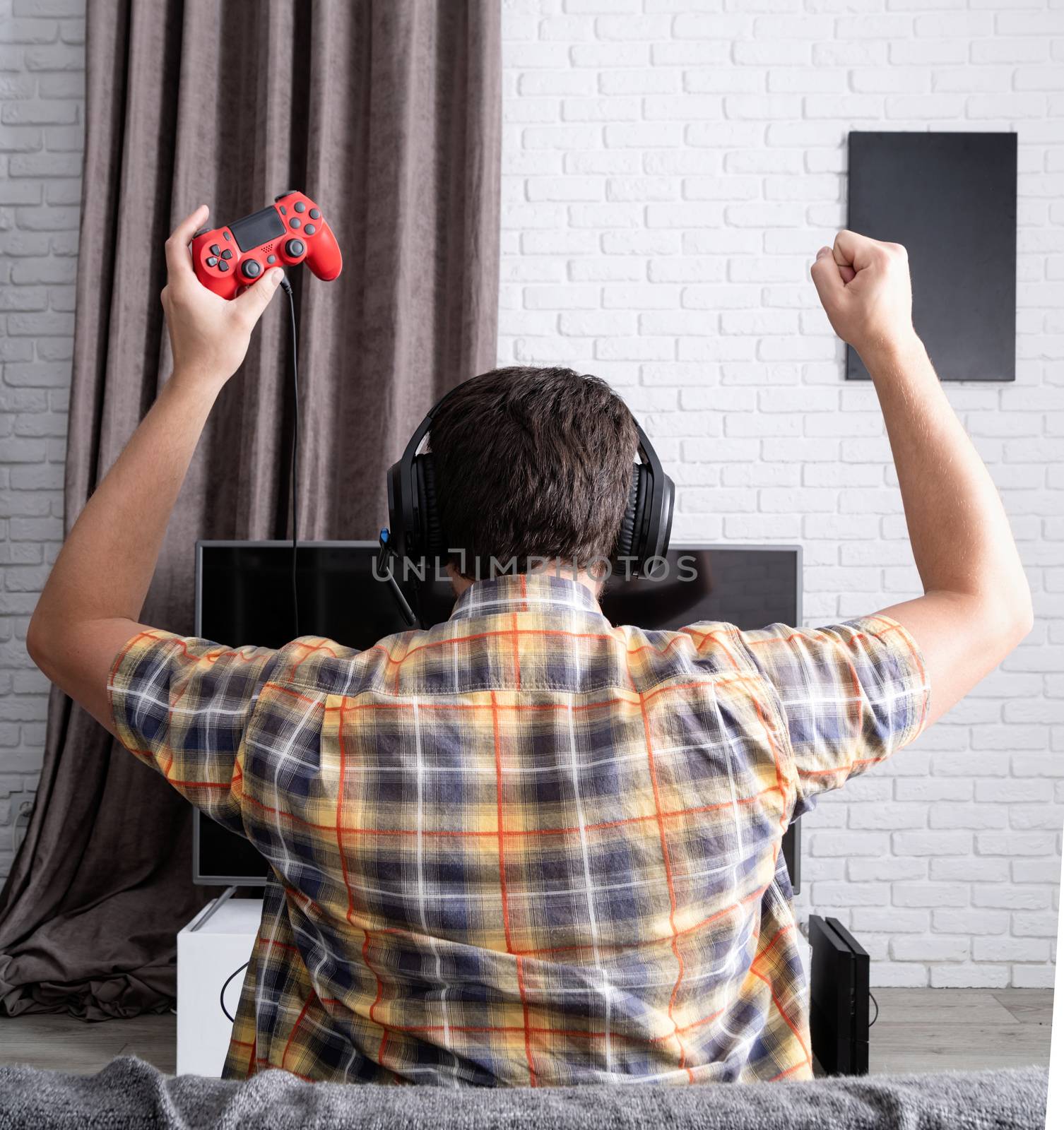 Rear view of a young man playing video games at home by Desperada