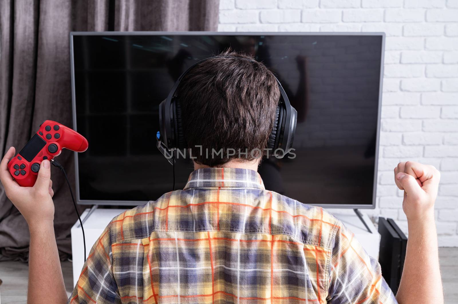 Rear view of a young man playing video games at home by Desperada