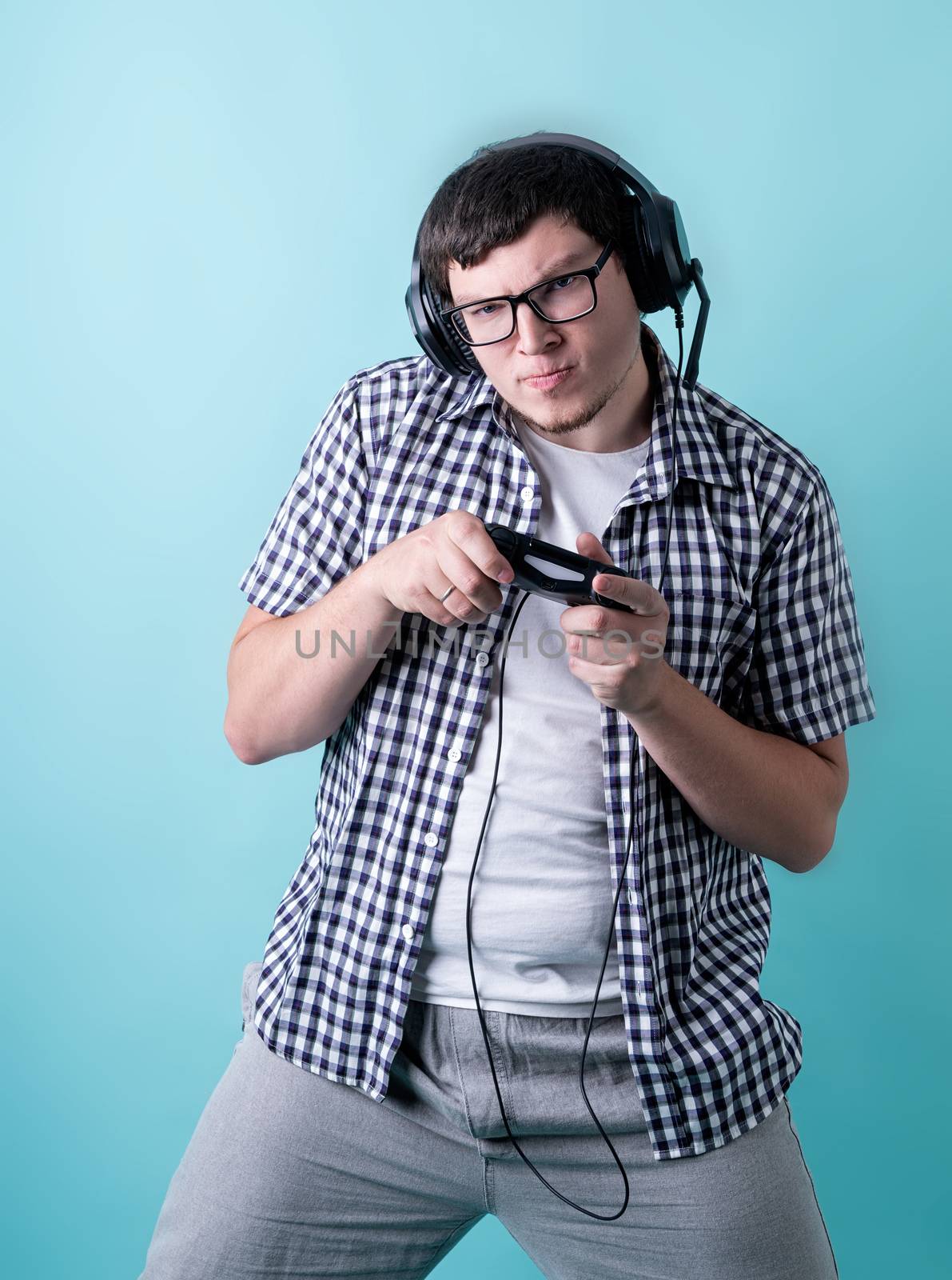 Funny young man playing video games holding a joystick isolated on blue background by Desperada