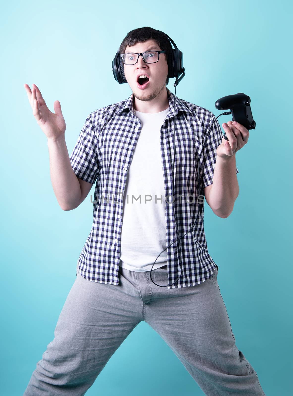 Shocked young man playing video games holding a joystick isolated on blue background by Desperada