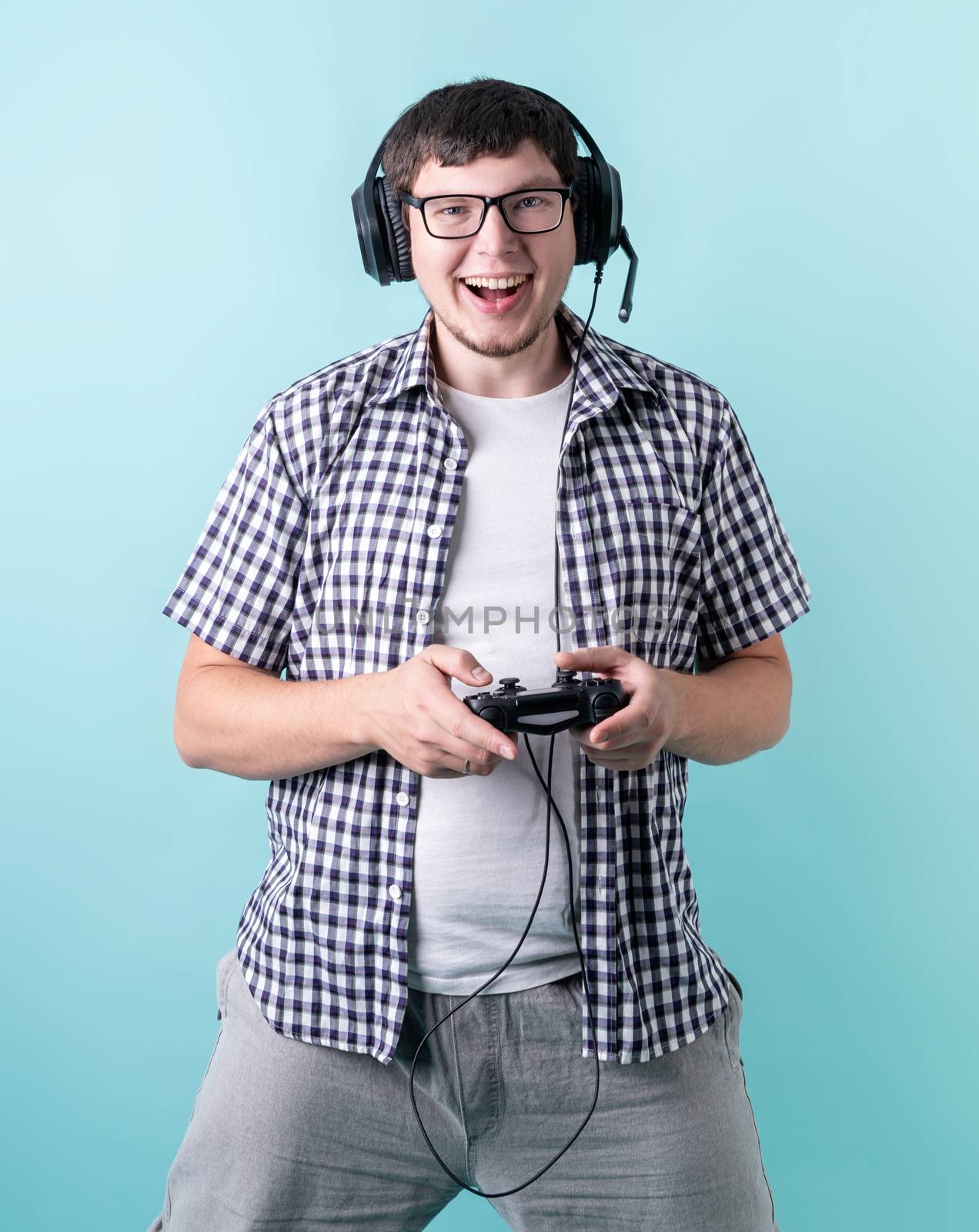 Happy laughing young man playing video games holding a joystick isolated on blue background by Desperada