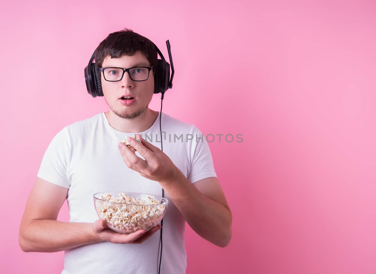 Stay home. Young mesmerized man watching a movie eating popcorn isolated on pink background with copy space