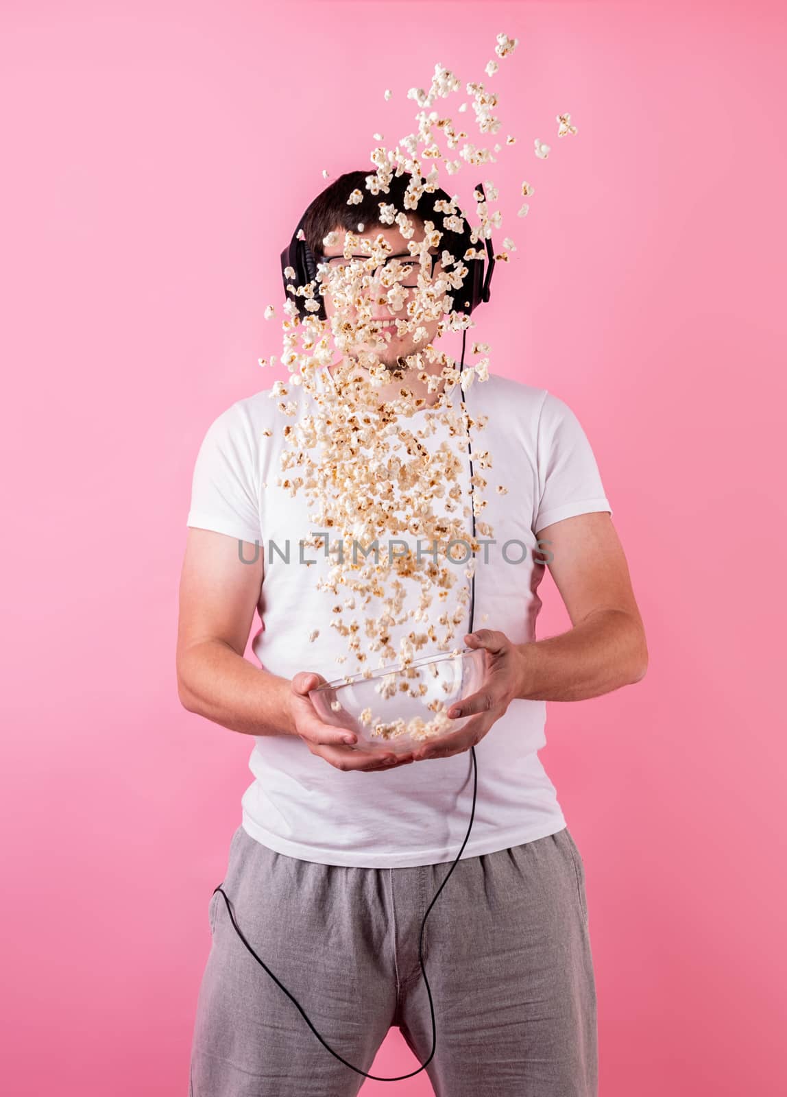 Young funny man throwing popcorn into the air isolated on pink by Desperada