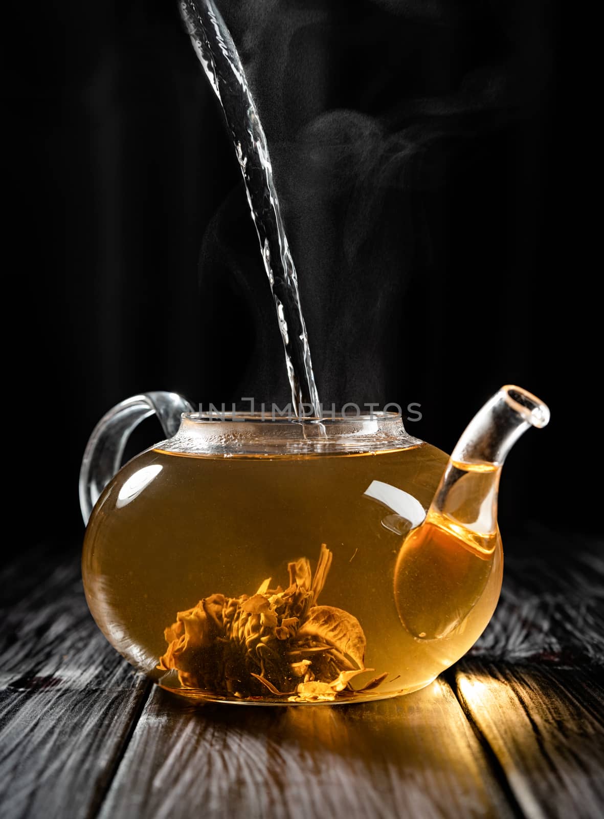 Brewing tea. Glass teapot with hot tea and steam. Hot water pouring into the teapot front view dark background
