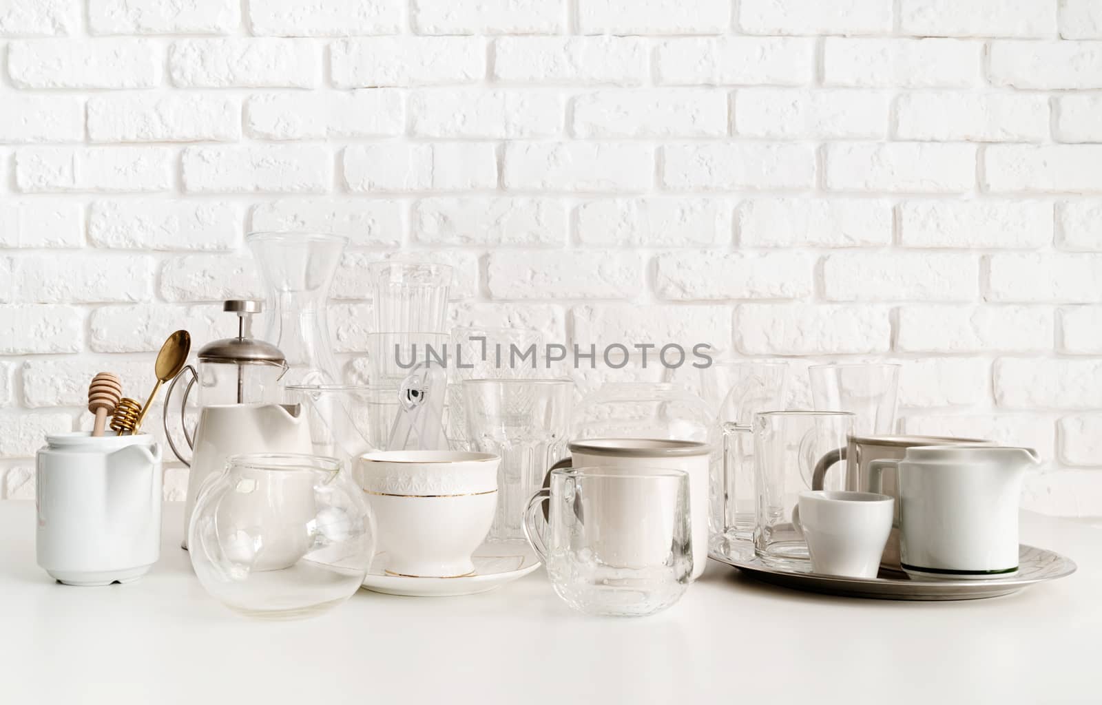ceramic and glass cups and tableware on the table on white brick wall background by Desperada
