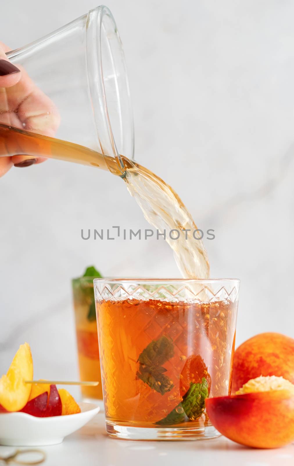 Jug with iced cold peach tea with fruit slices and mint. Iced cold peach tea poured into the glass