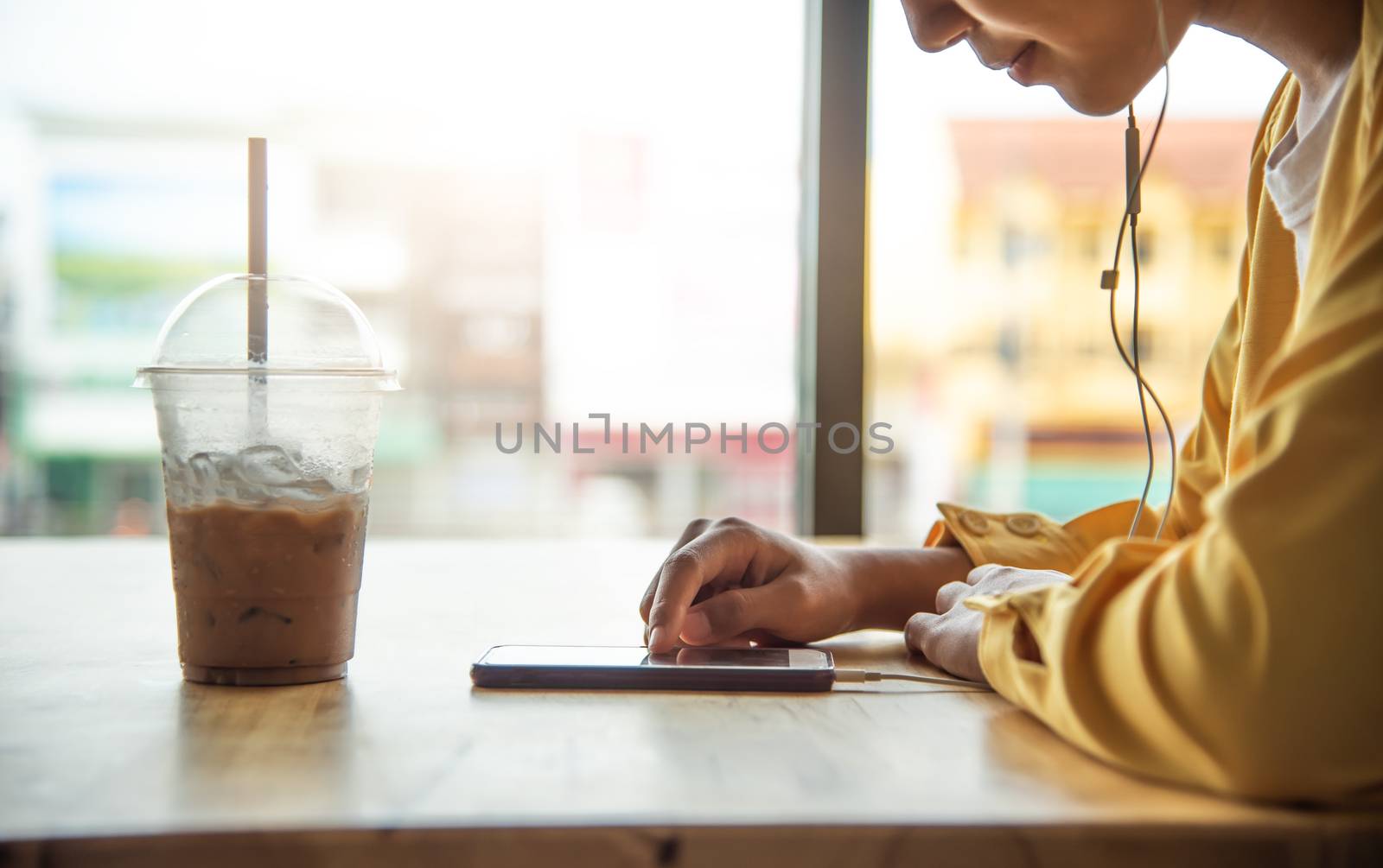 The girl is enjoying the phone in coffee cafe and have a glass of cold drink in a foreground