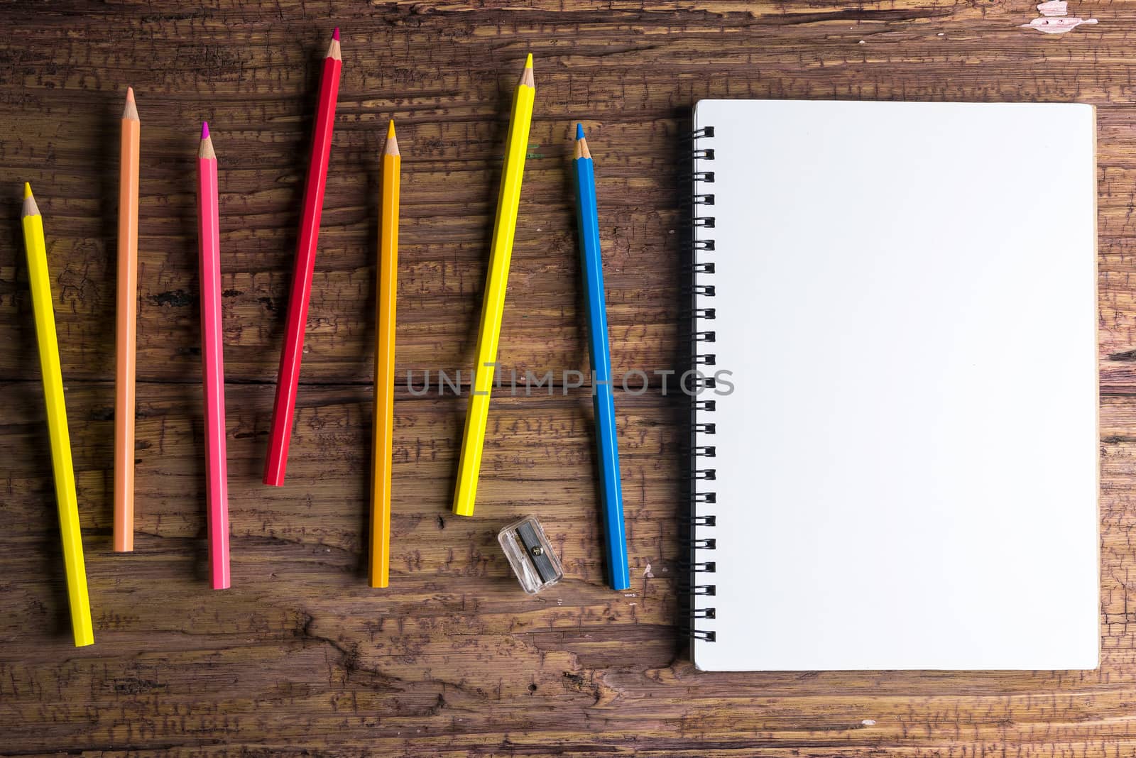 Top view of Blank notebook white paper and variegated colored pencils on brown wooden background with space for your message