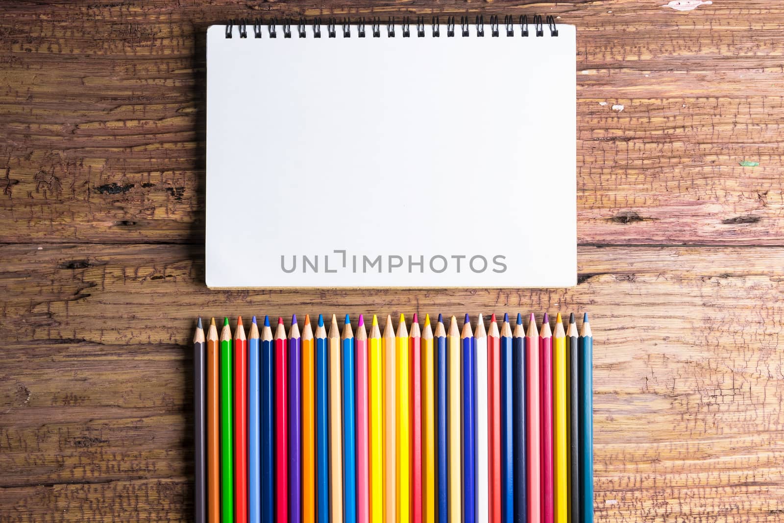 Top view of Blank notebook white paper and variegated colored pencils on brown wooden background with space for your message