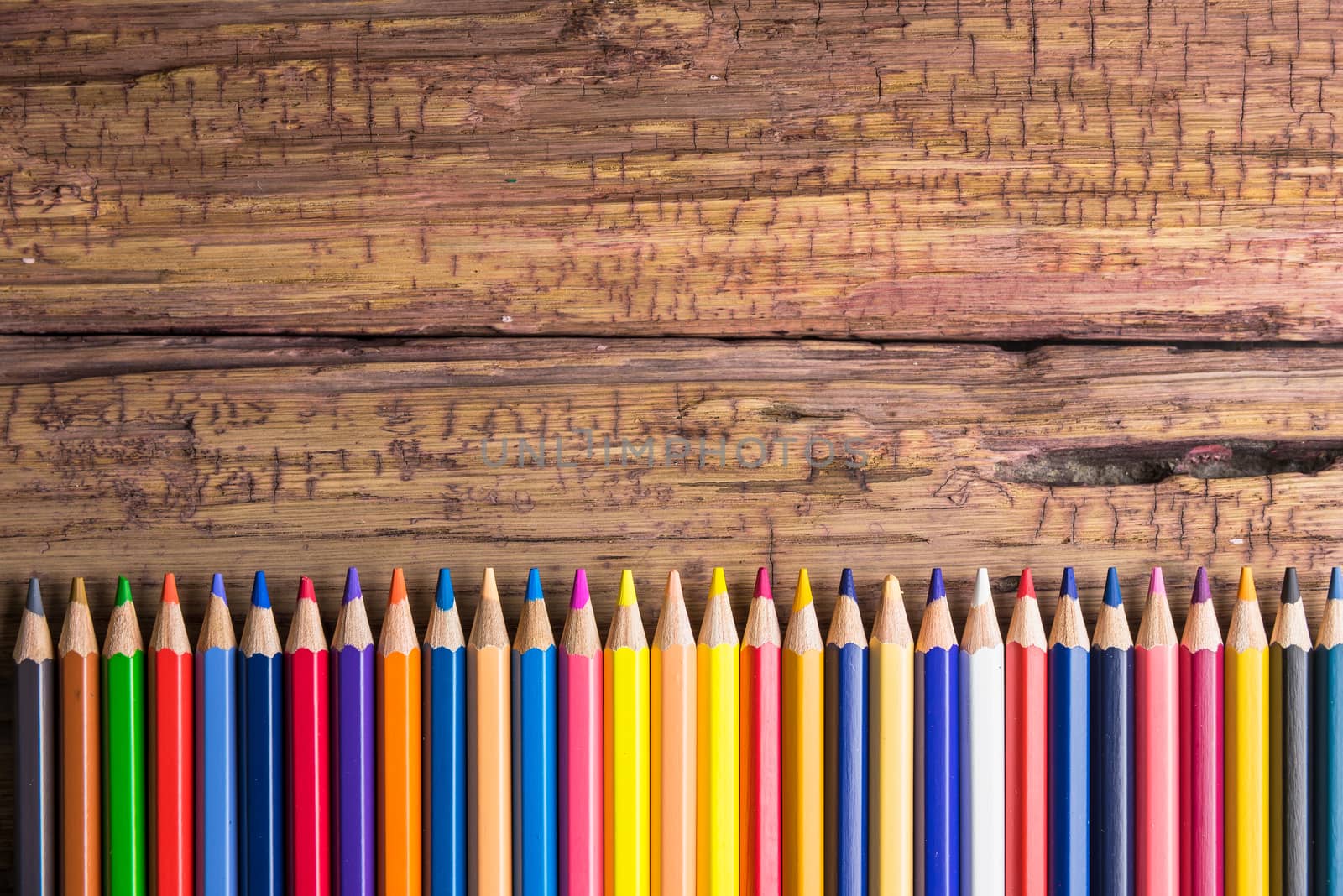 Top view of a set of colored pencils on wooden background with space for your message