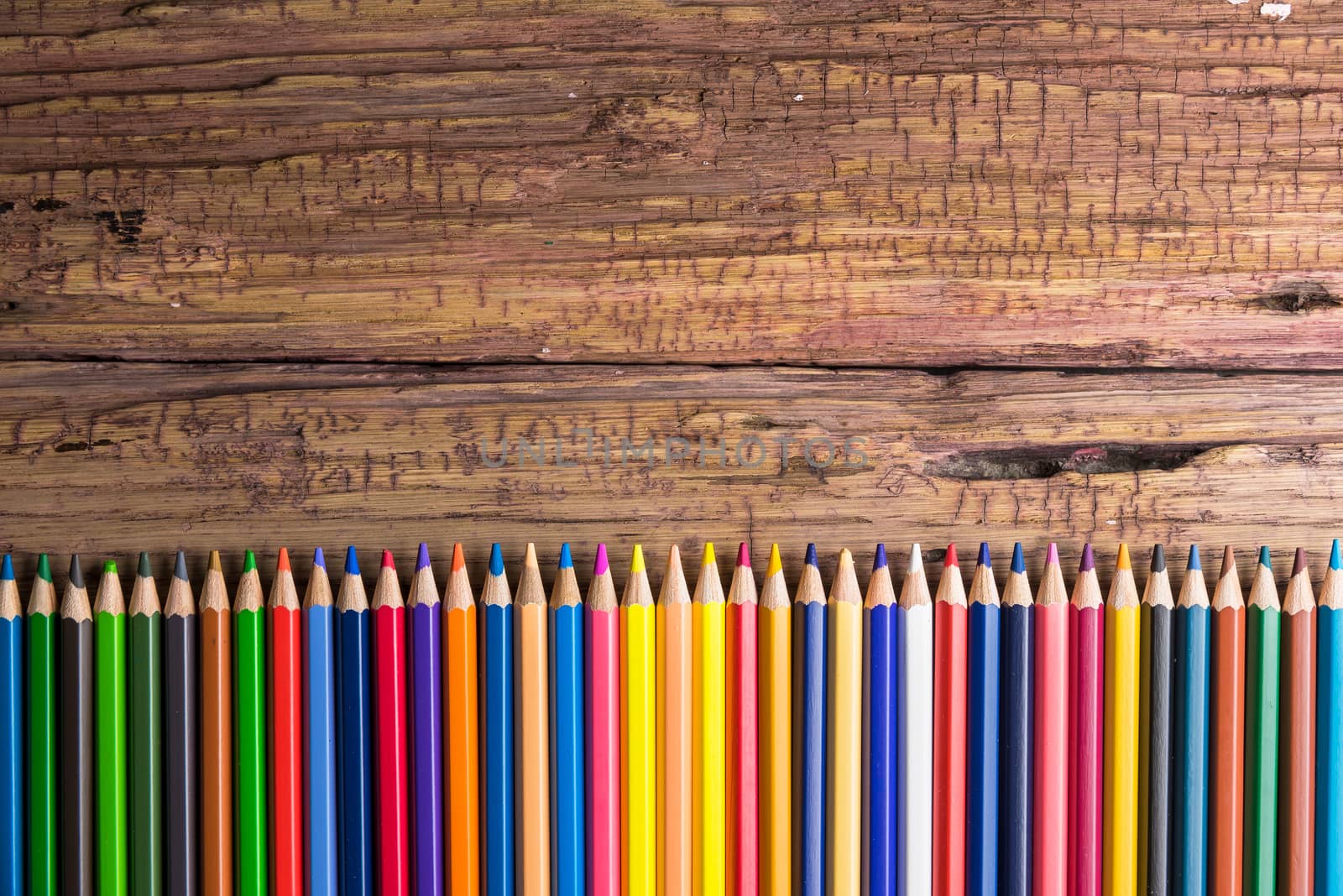 Top view of a set of colored pencils on wooden background with space for your message