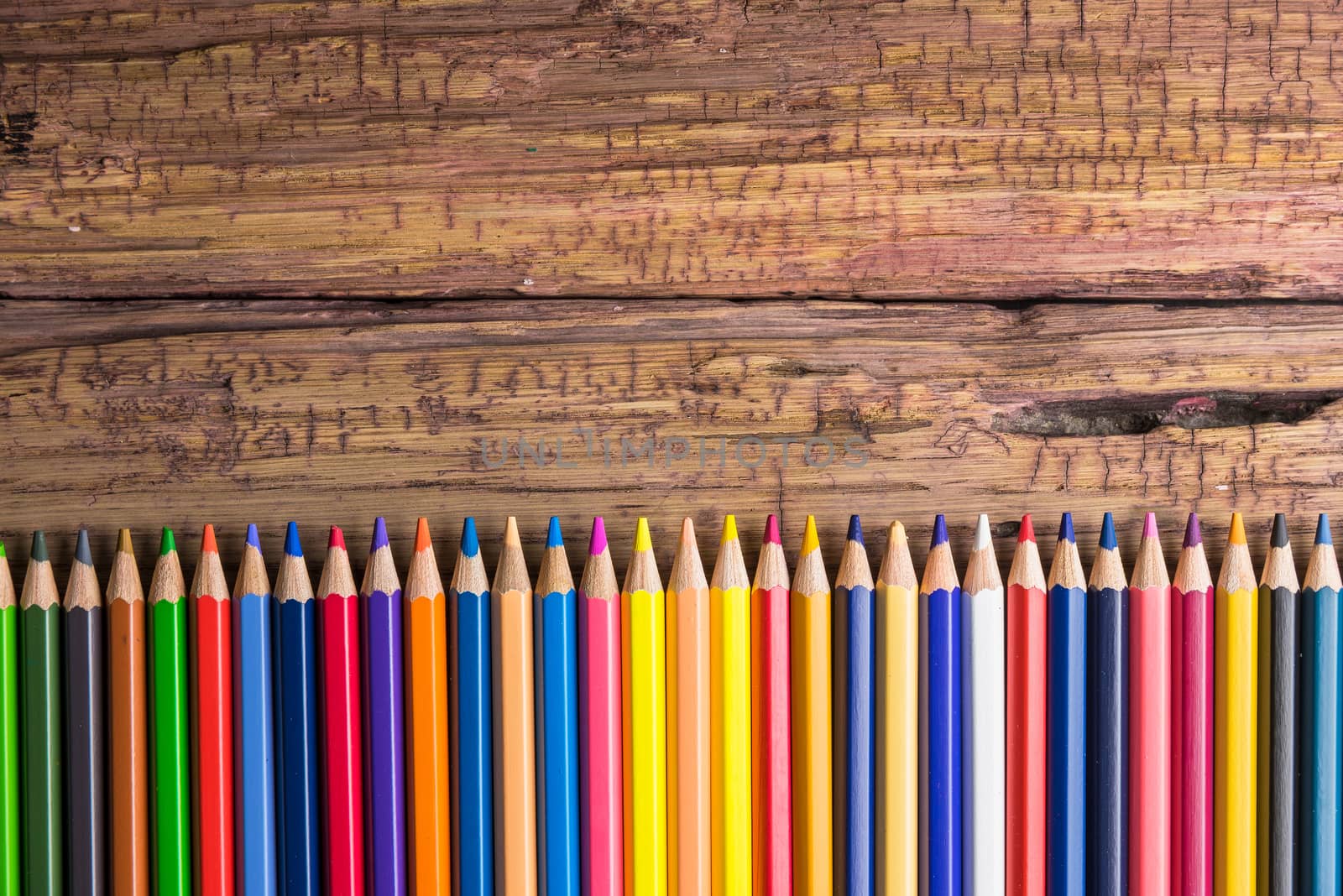 Top view of a set of colored pencils on wooden background with space for your message