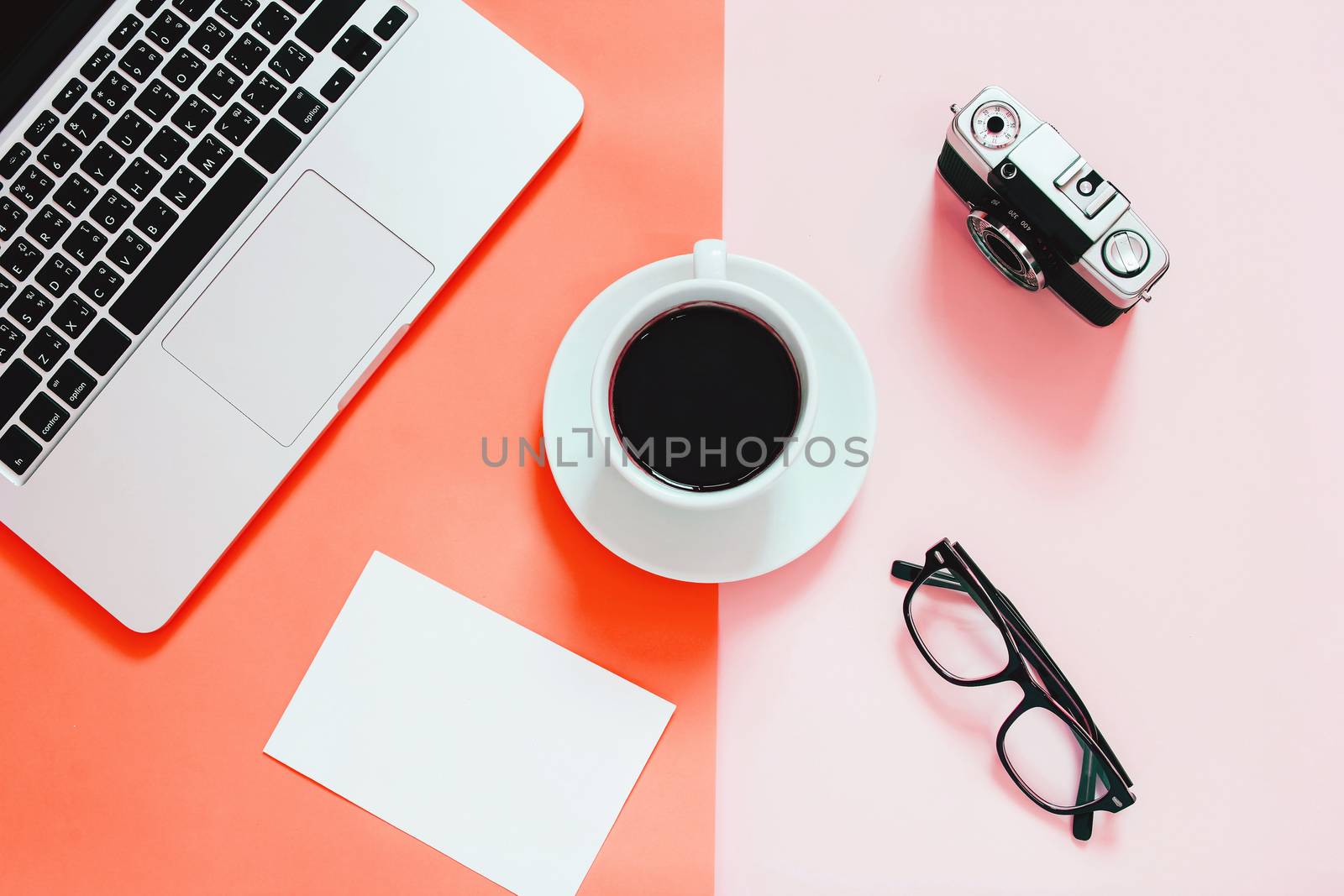 Living Coral color background, Color of the year 2019, flat lay of workspace desk with laptop, blank paper, coffee, eyeglasses and camera 
