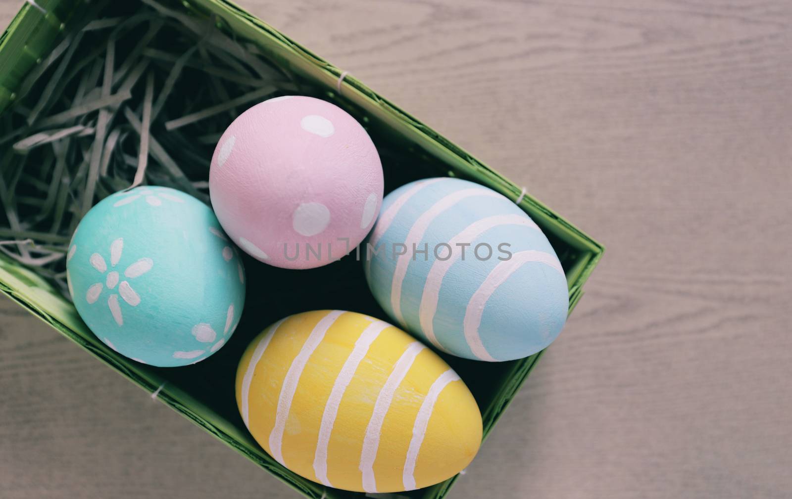 Pastel and colorful easter eggs in nest and basket on wooden background and copy space, happy easter holiday concept