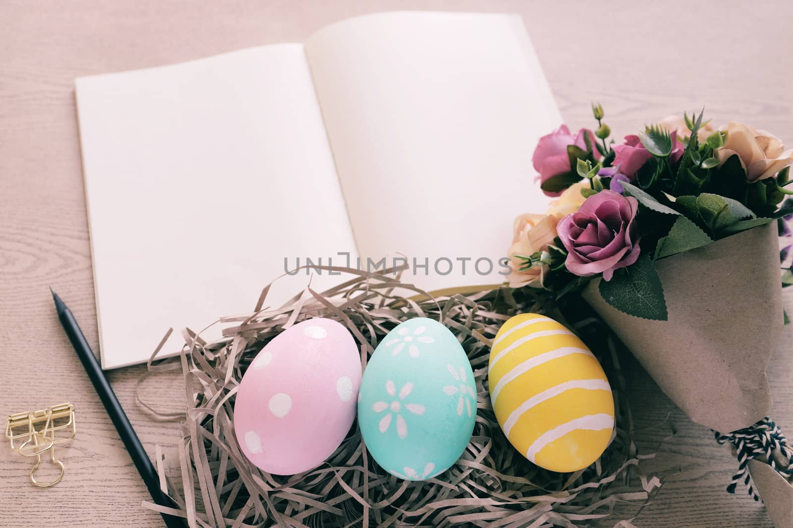 Pastel and colorful easter eggs in nest and bouquet of flower with blank notebook on wooden background, happy easter holiday concept