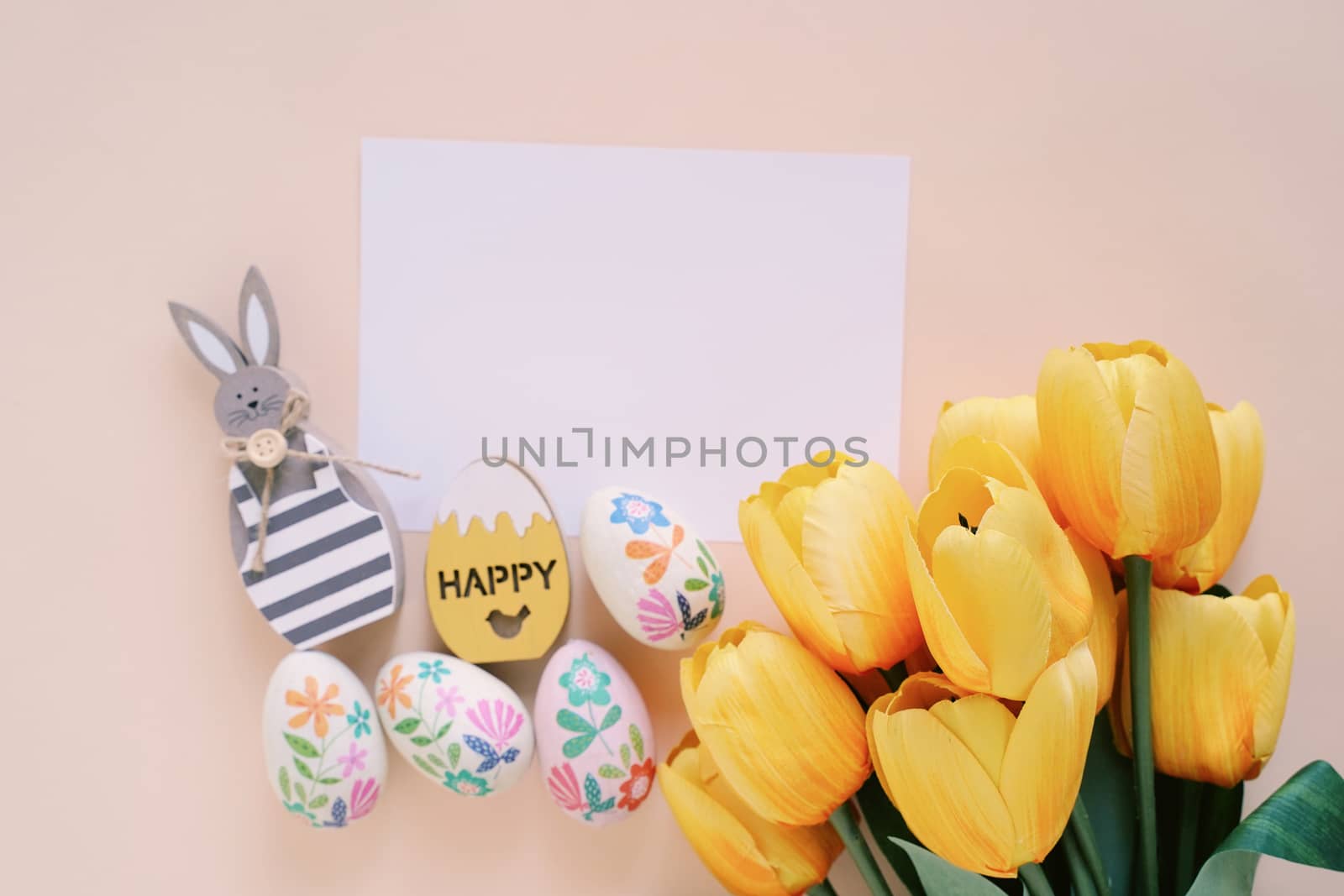 Happy Easter concept with blank card, wooden bunny, colorful easter eggs and yellow tulips. Top view with copy space