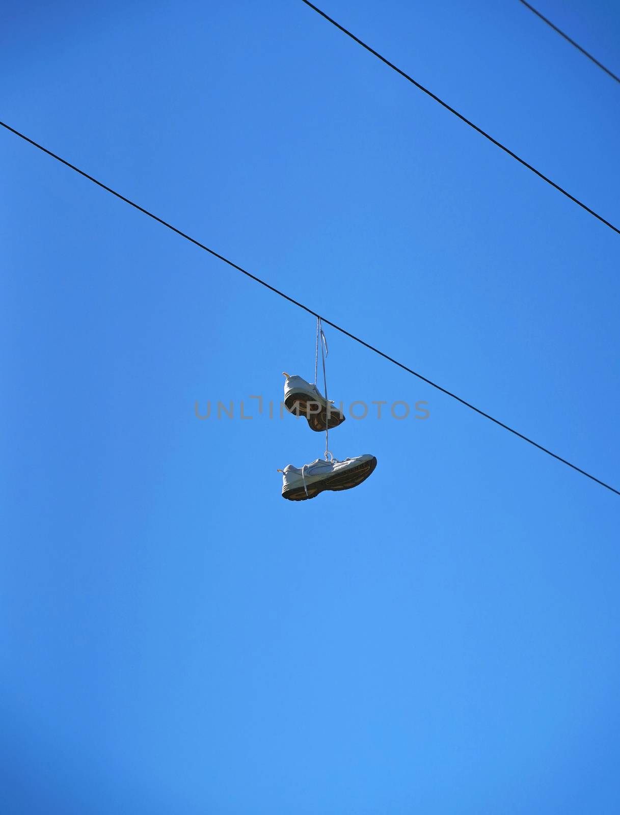 Old sneaker shoes hanging on an electric cable against blue sky