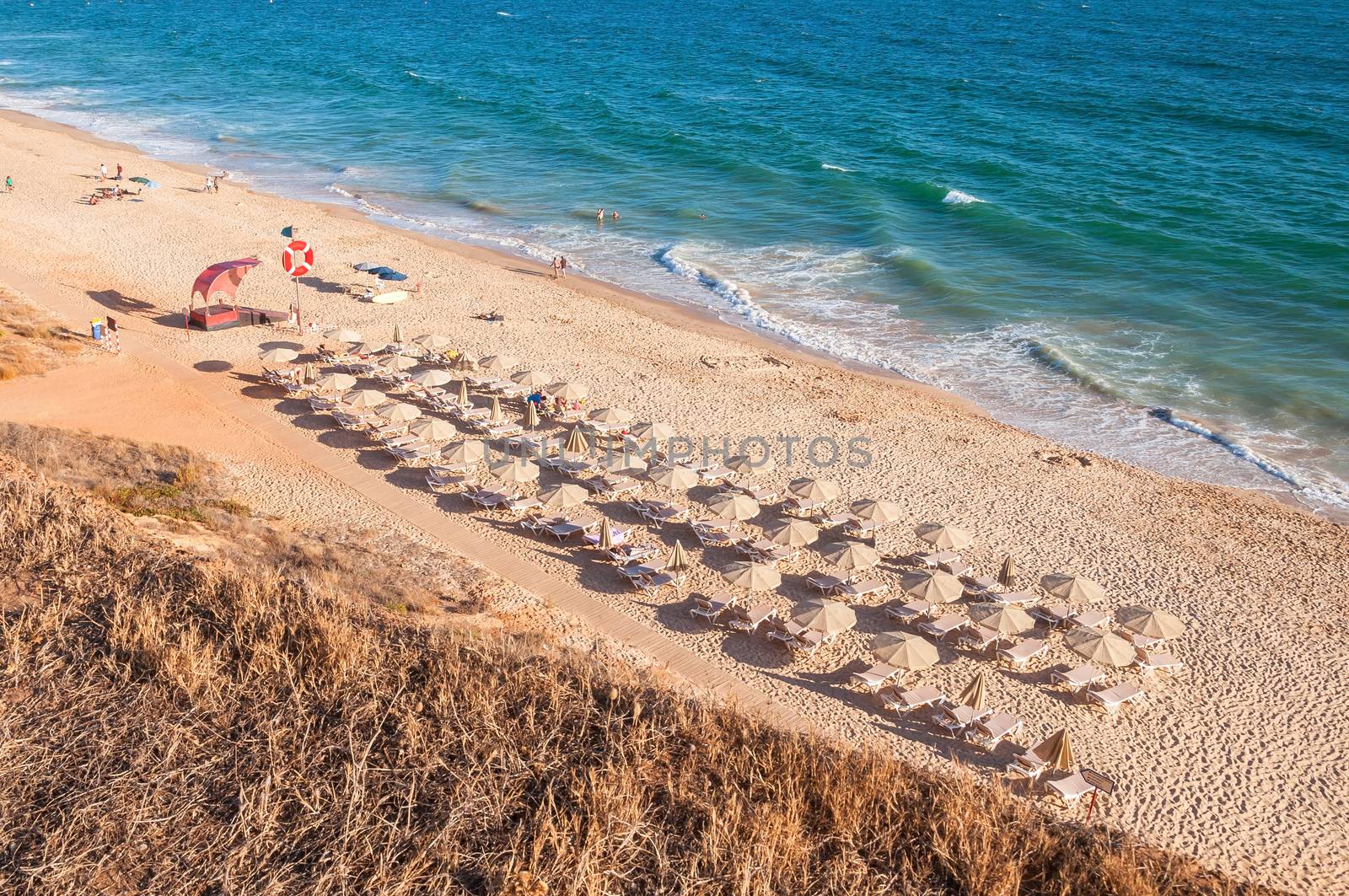 Sunbeds and umbrellas on the Falesia Beach in afternoon sun, Algarve, Portugal