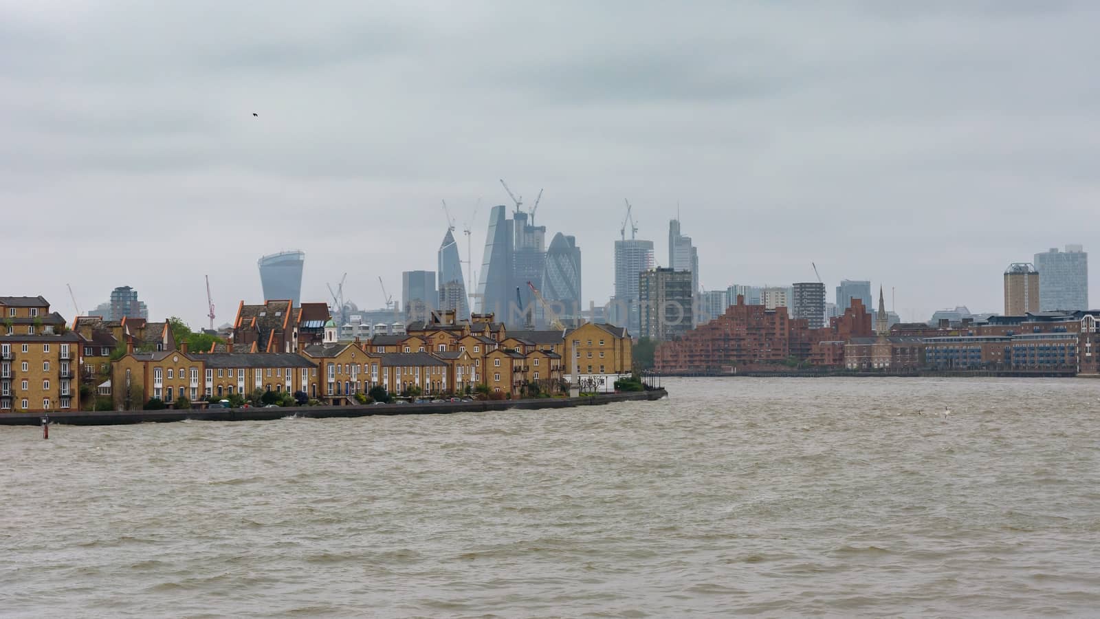 View of River Thames in London docklands with city skyscrapers in the background on a cloudy day