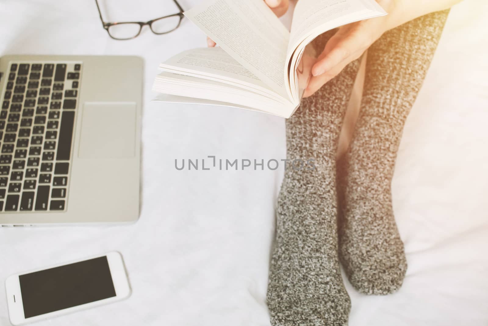 Top view of woman legs in socks reading a book and using laptop  by nuchylee