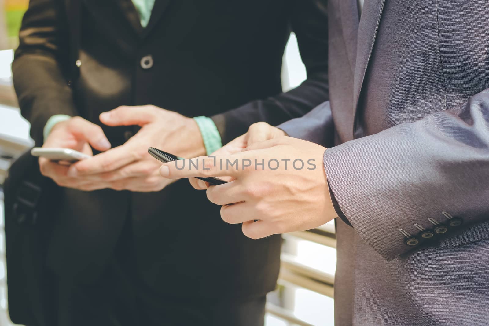 Midsection of two colleague businessmen using smartphone, business and technology concept