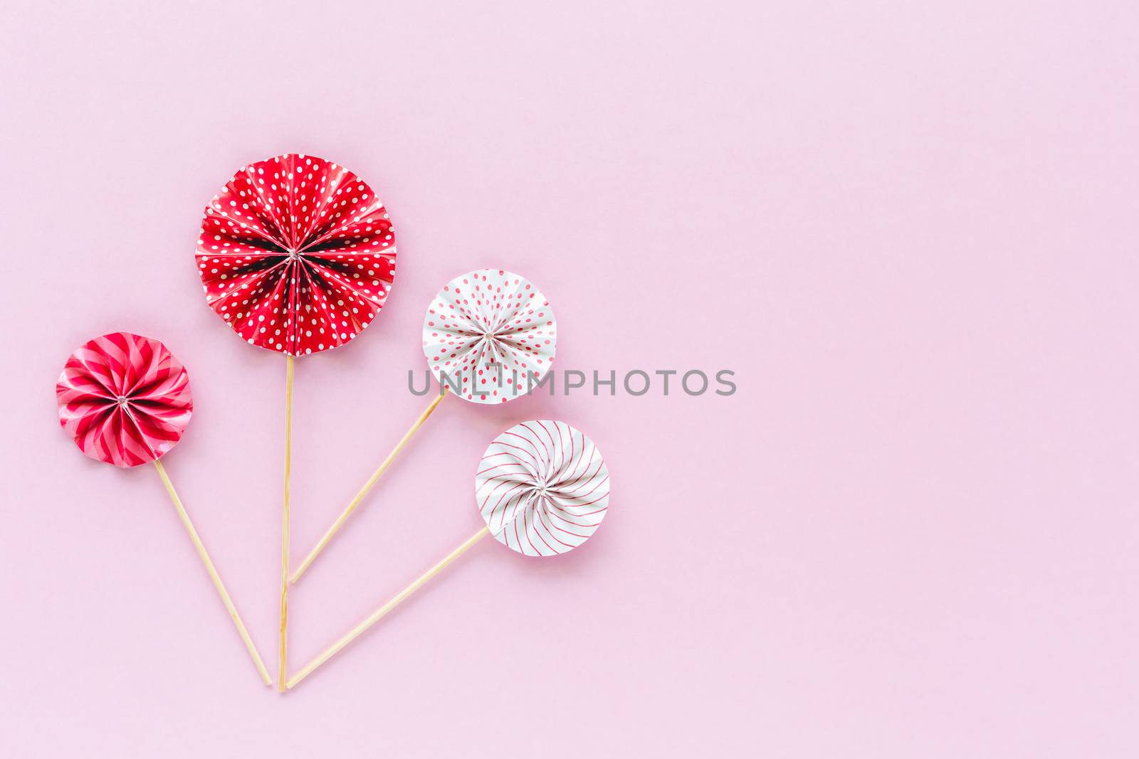 Red and white paper fan with wooden stick on pink background for party decoration