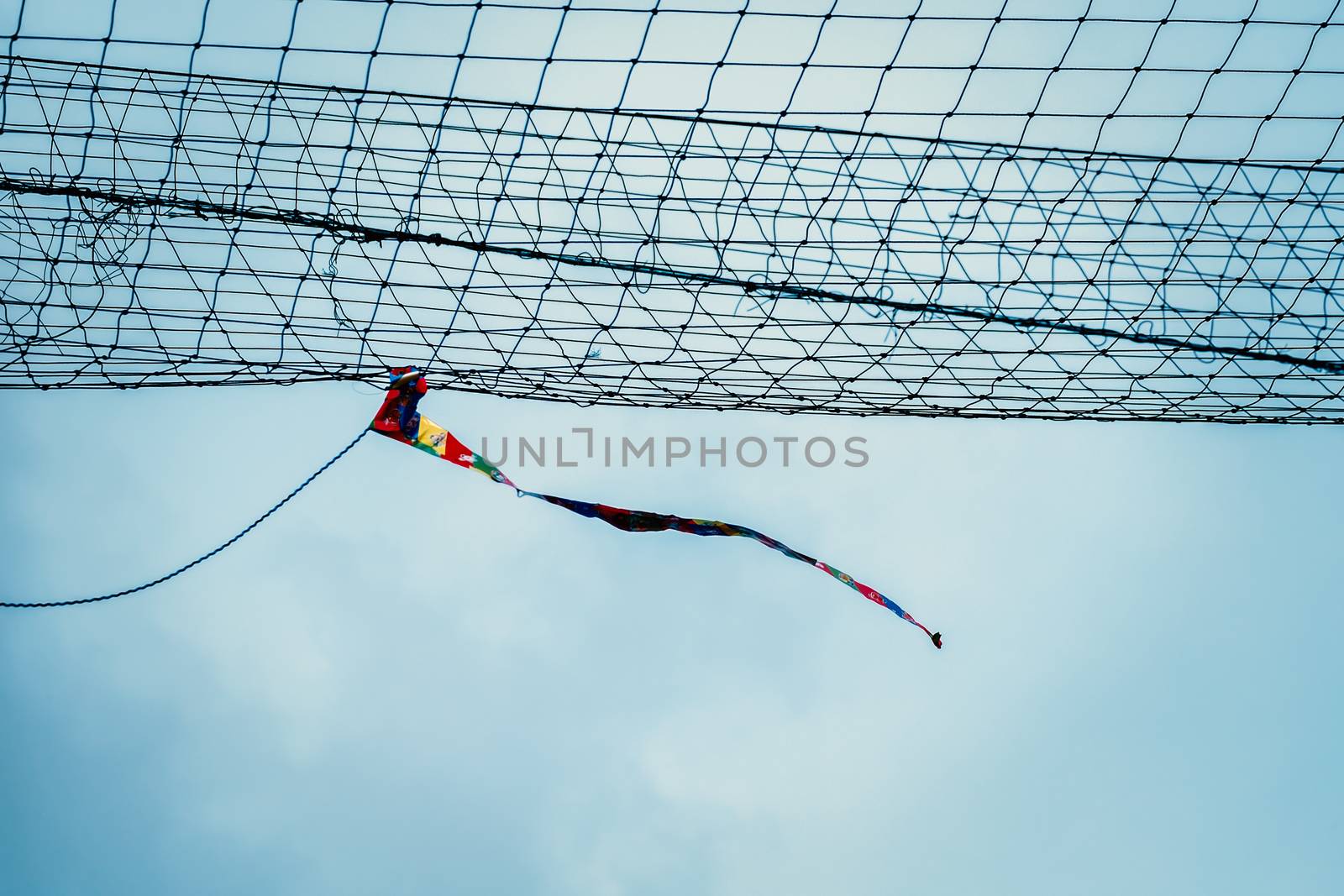 Rag tied to the net blowing in sport field similar to windsock to show the direction and strength of the wind against cloudy sky in the blue day