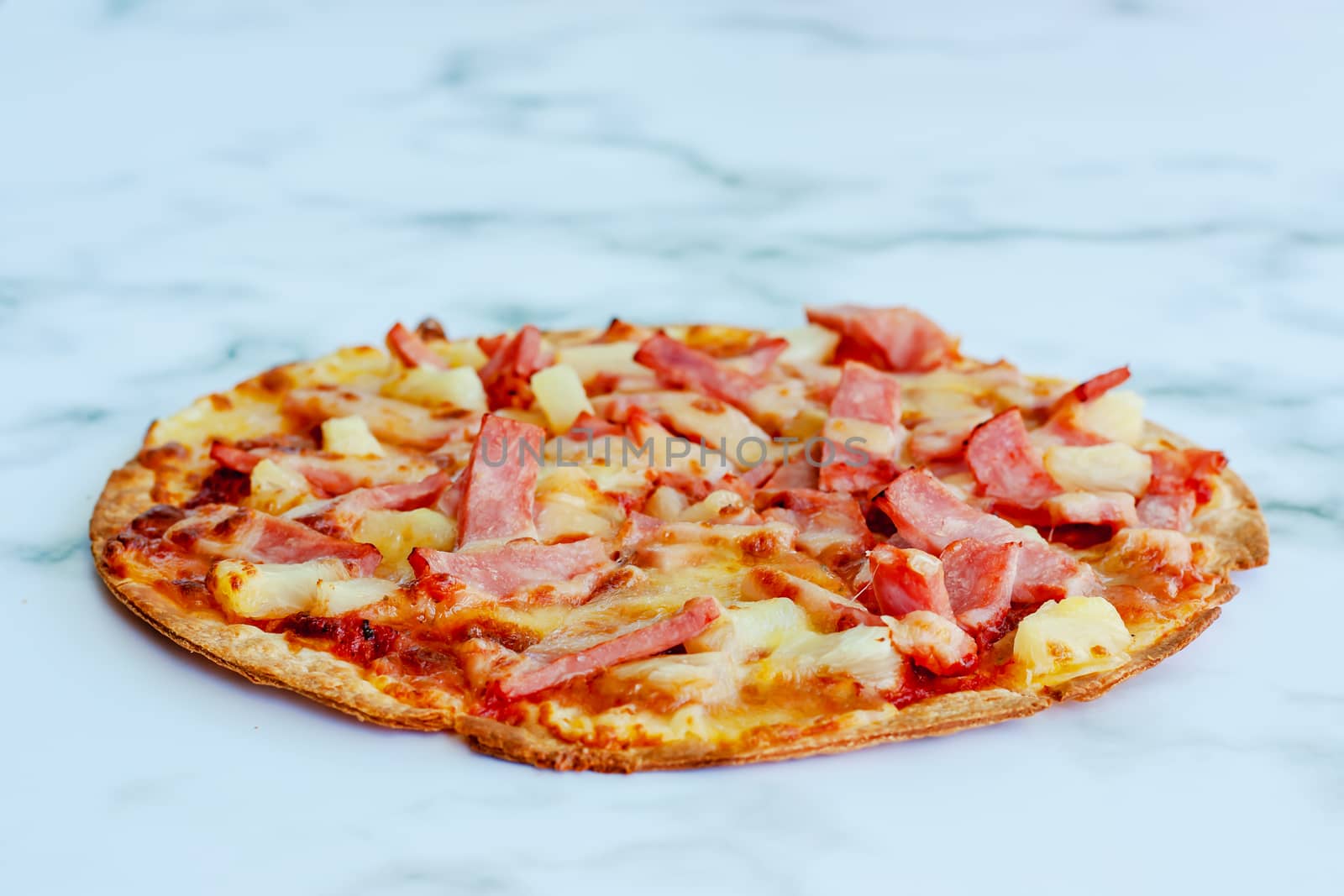 Delicious pizza with pineapple, ham slice, bacon slice, mozzarella cheese, pizza sauce on white marble background for fast food and ready to eat concept
