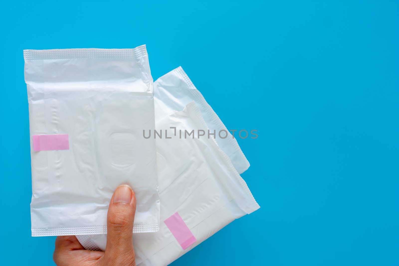 Hand holding feminine sanitary napkin, an absorbent item worn by a woman while menstruating, on blue background for hygiene and health concept