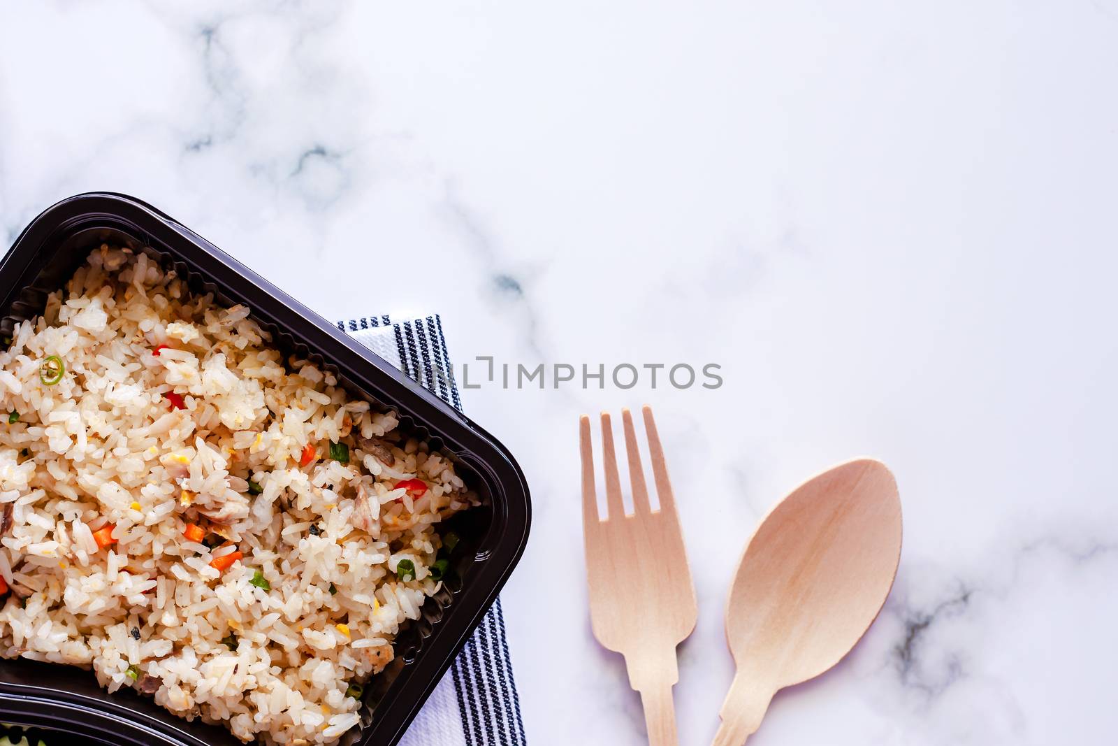 Delicious fried rice in lunch box with napery, wooden spoon and fork on marble background for ready to eat and food concept