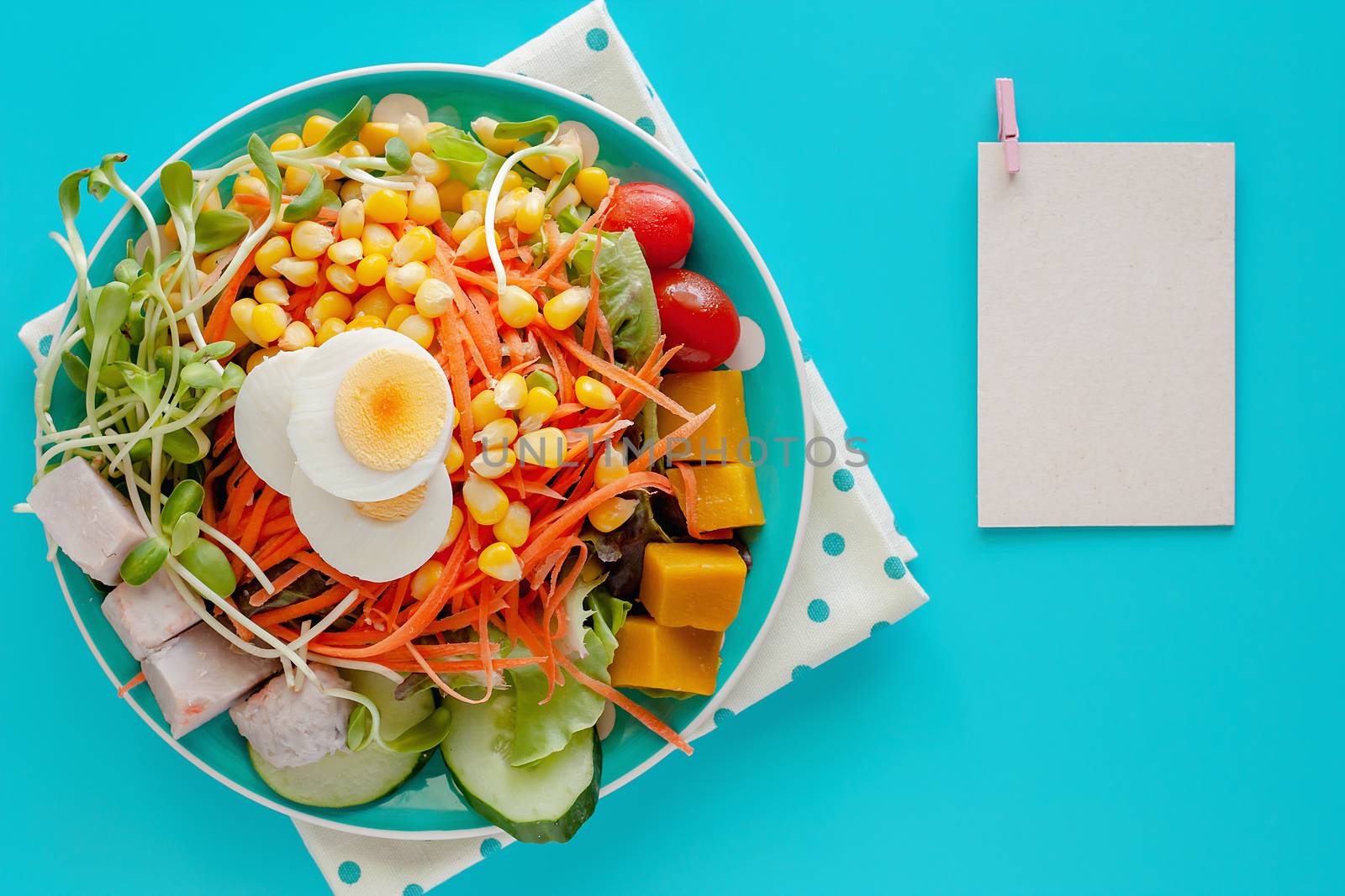 Fresh salad vegetable with boiled chicken egg and blank note paper on blue background for healthy eating and diet food concept